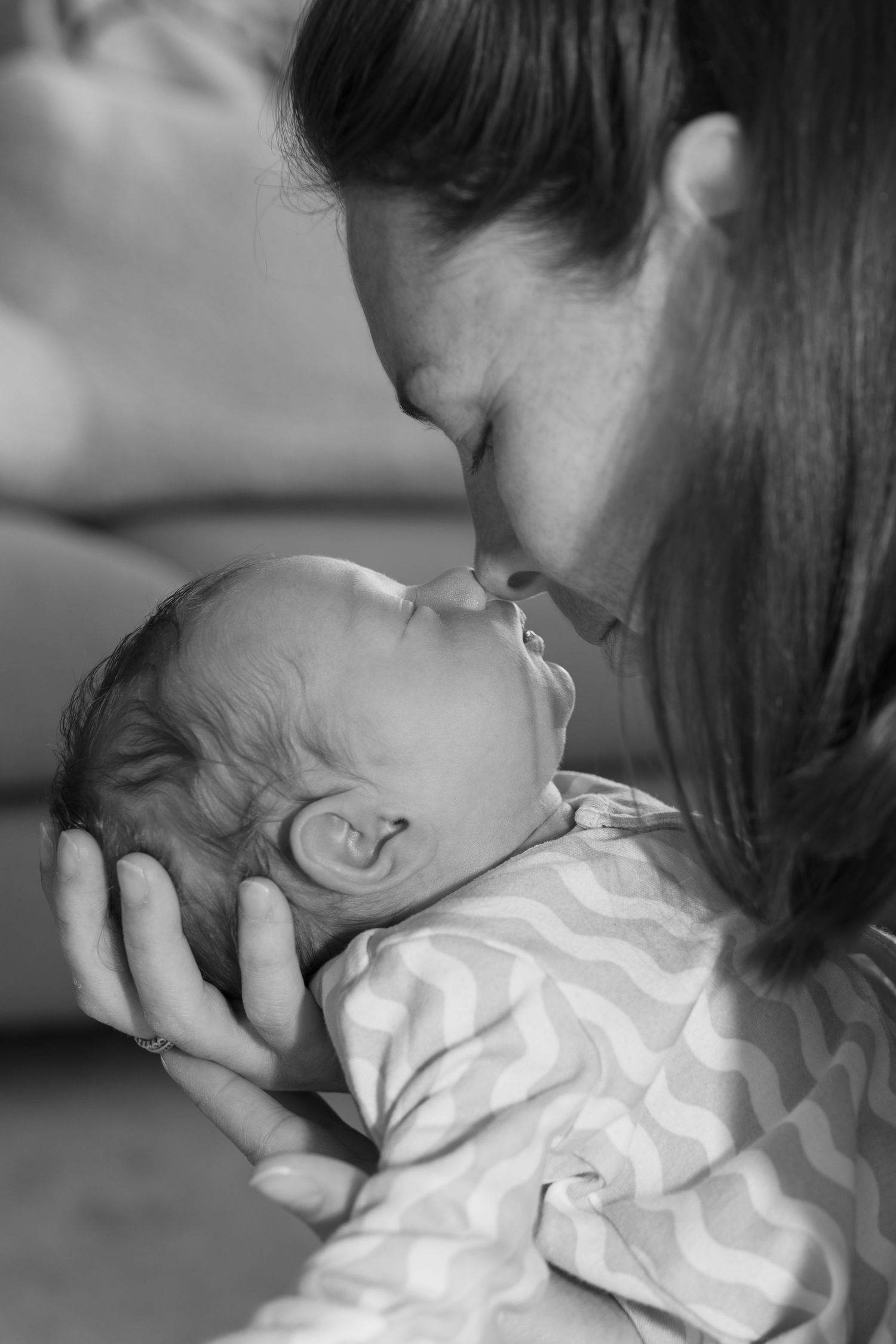 Black and white photo of a mother tenderly kissing her newborn baby while cradling its head in her hands.