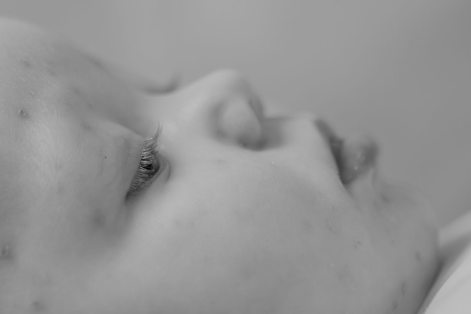 Close-up black and white profile portrait of a newborn baby lying down with delicate features.