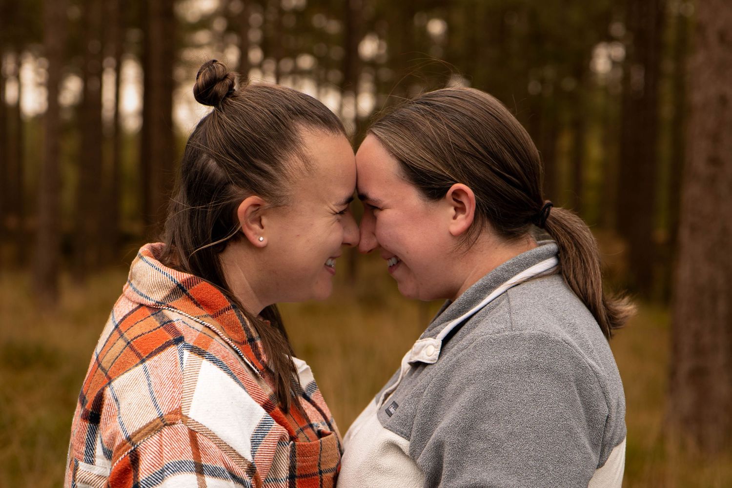 Two women touching foreheads and smiling softly in a tender forest couples portrait.