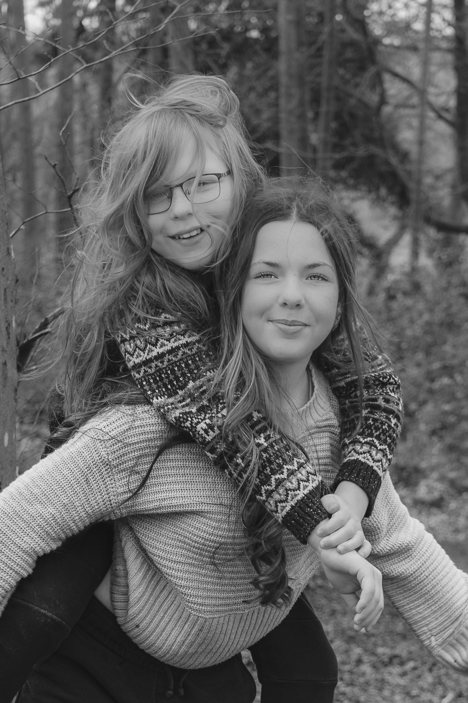 Black and white photo of two sisters smiling outdoors, one giving the other a piggyback ride.