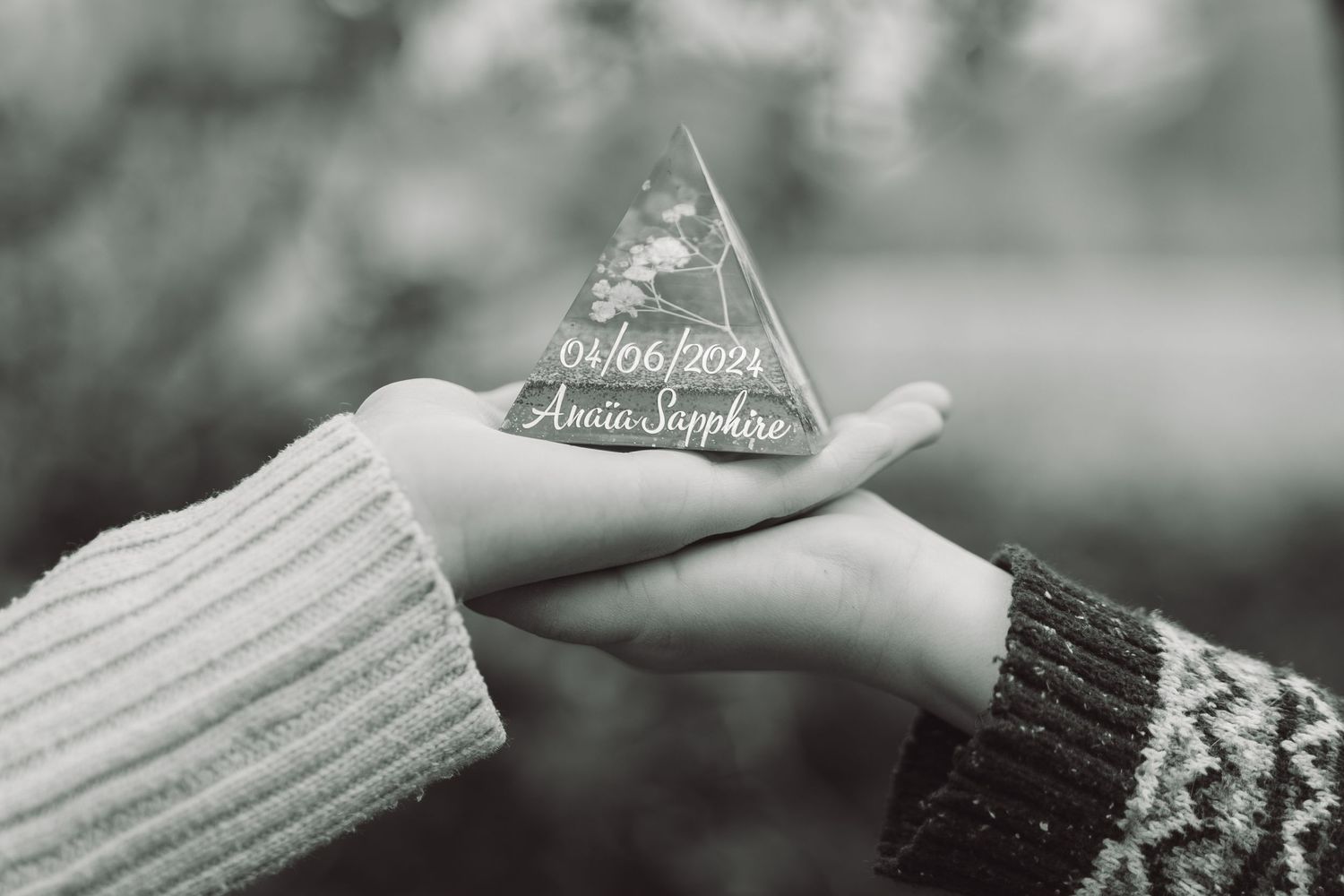 Hands holding a triangular glass keepsake engraved with the name Amaia Sapphire and a date.