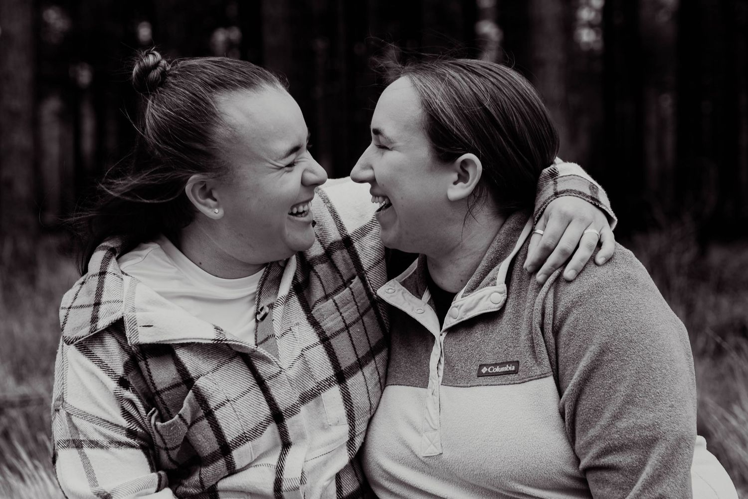 Two women smiling and embracing nose-to-nose in a joyful black and white outdoor portrait.