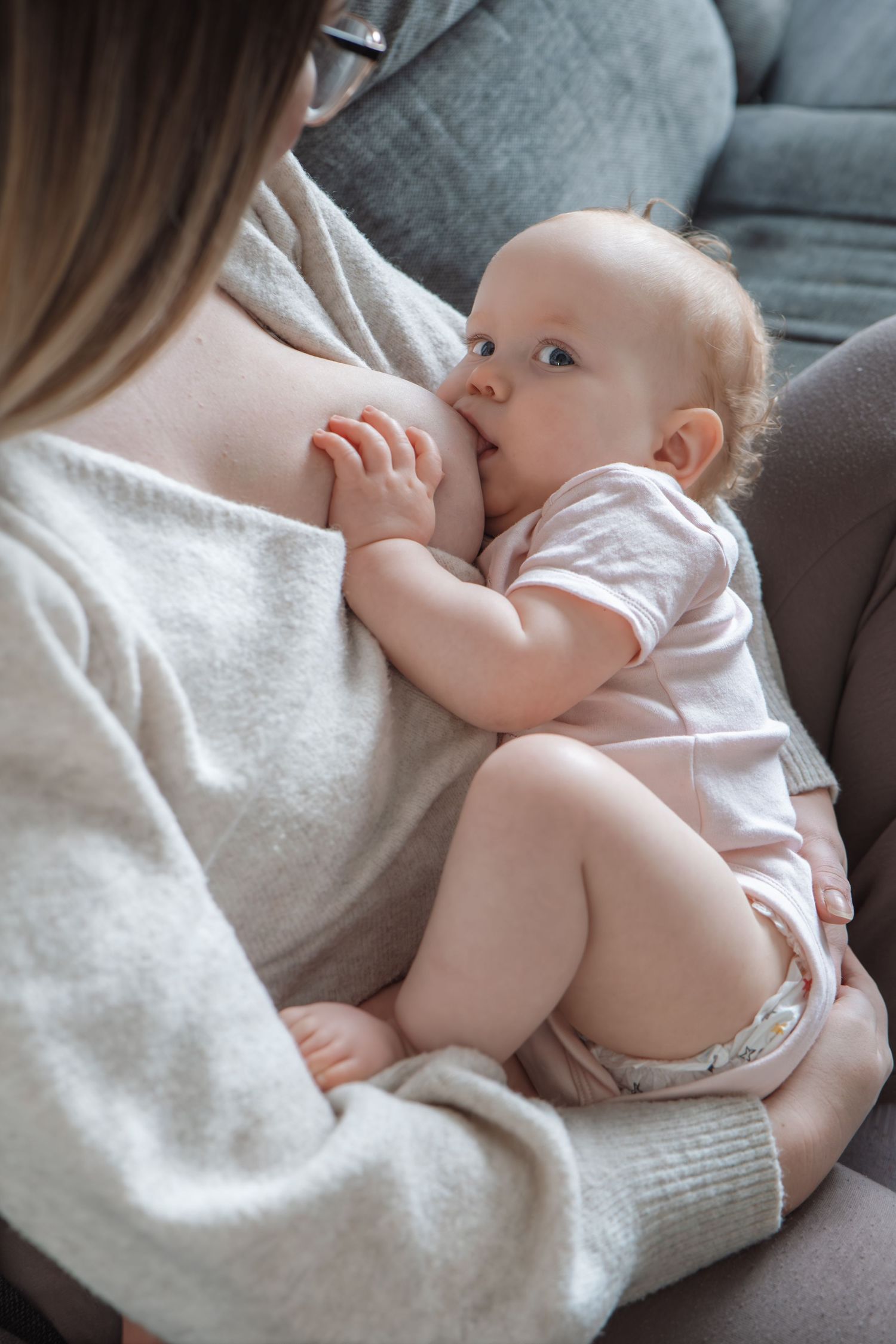 A mother breastfeeding her infant baby while sitting on a couch at home.