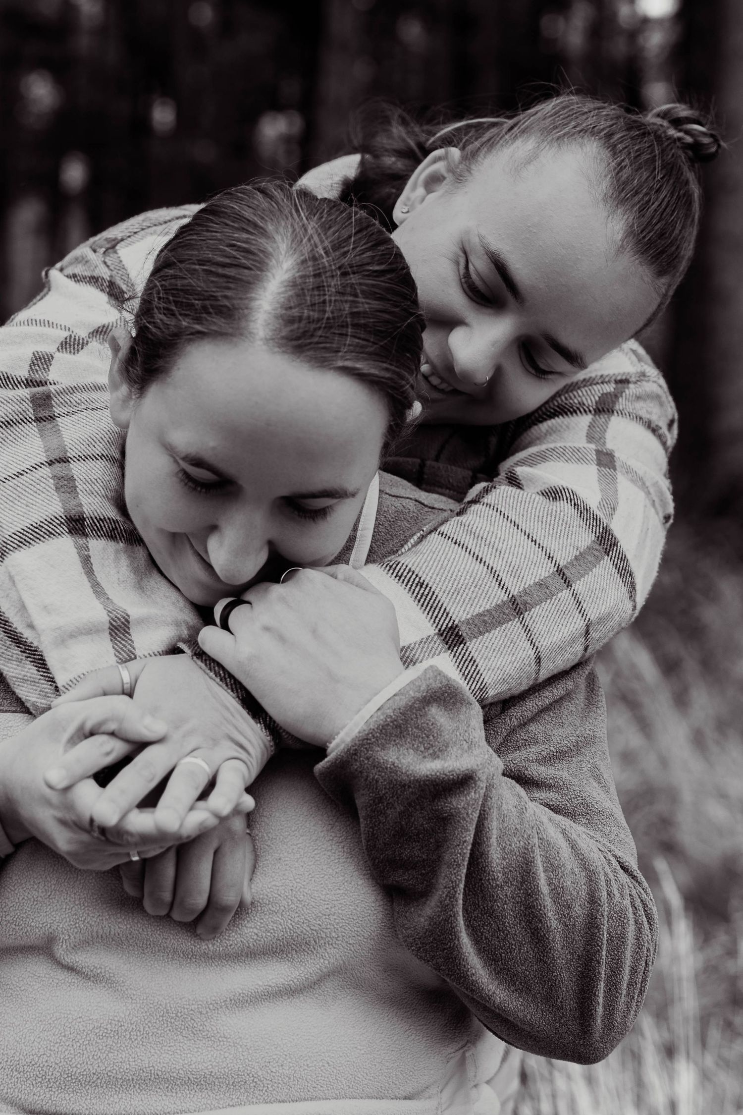 Woman hugging her partner from behind tenderly in a black and white forest portrait.