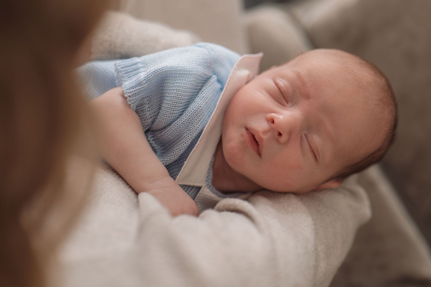 Sleeping newborn baby in a blue knit outfit cradled in loving arms.