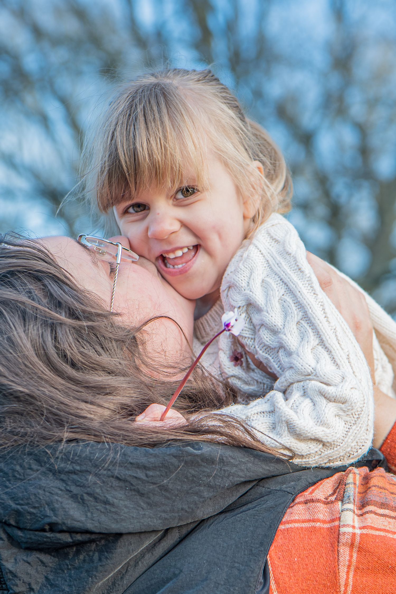Joyful young girl laughing while being held by a parent outdoors in winter.