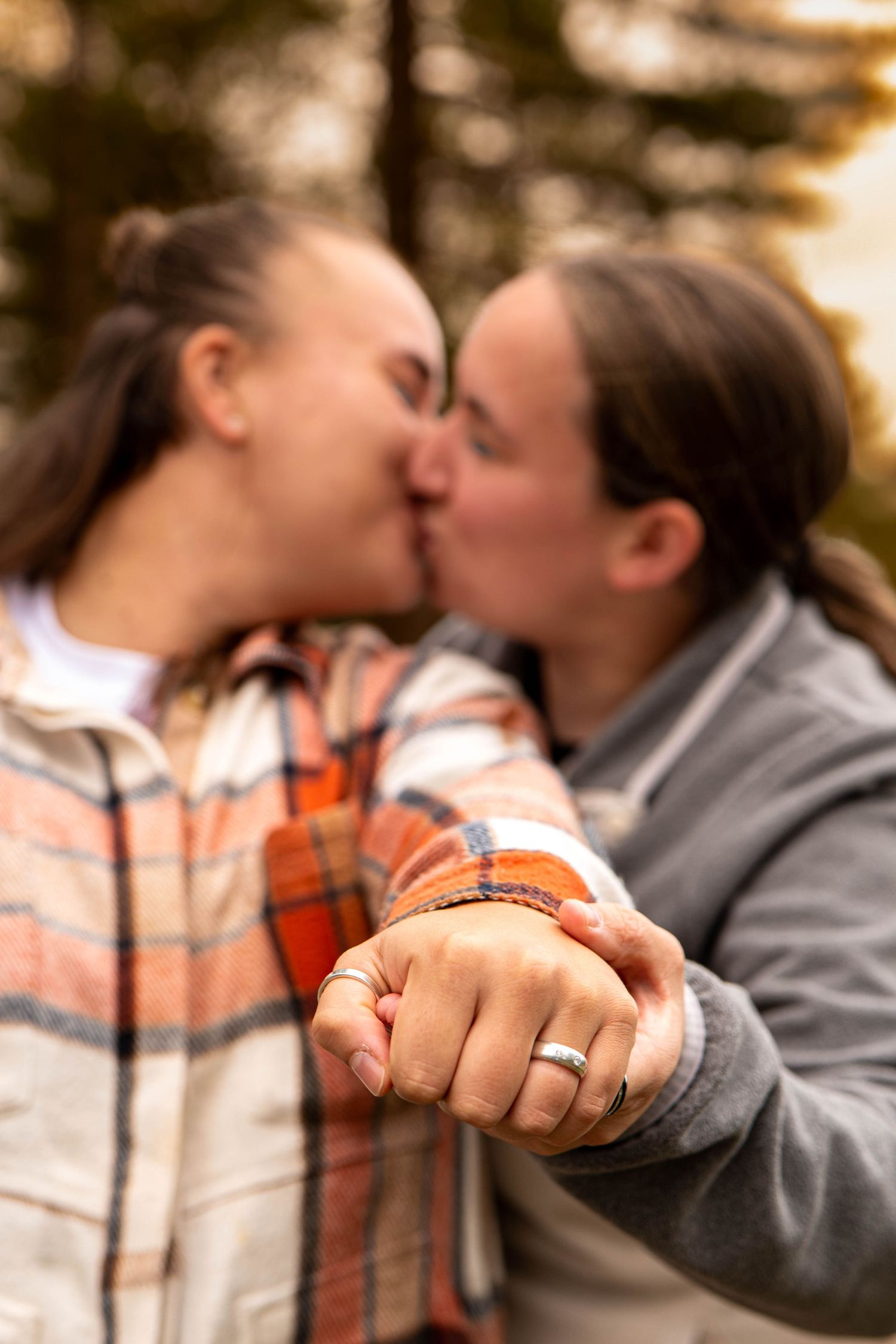 Engaged couple kissing while displaying their matching rings in a romantic forest engagement photo.