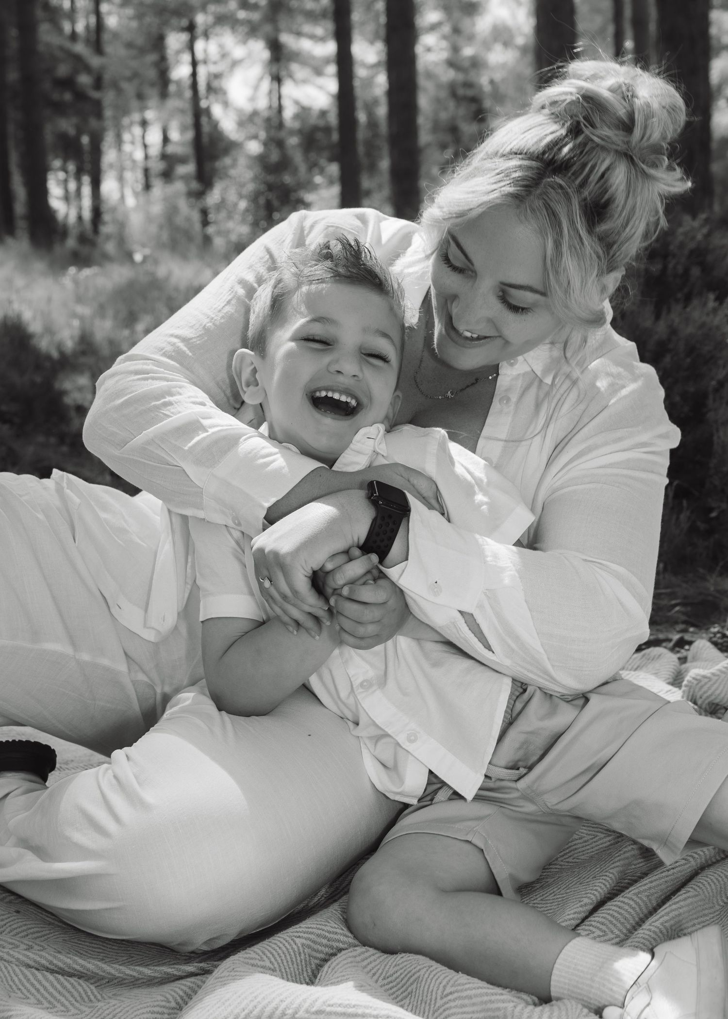 Candid black and white photo of a mum and son laughing and tickling