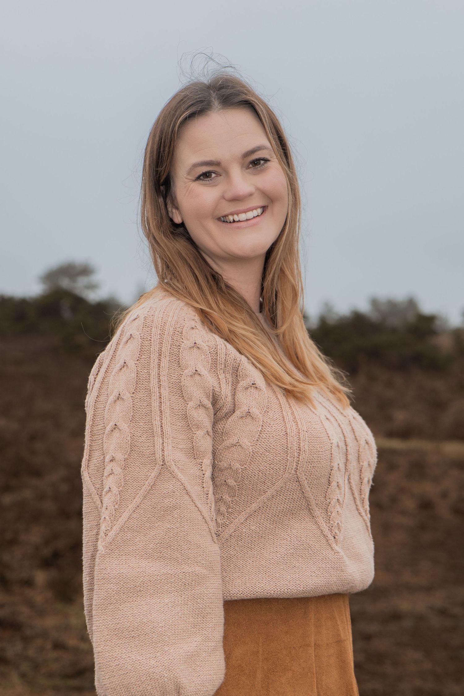 Smiling young woman with long hair wearing a beige knit sweater outdoors.