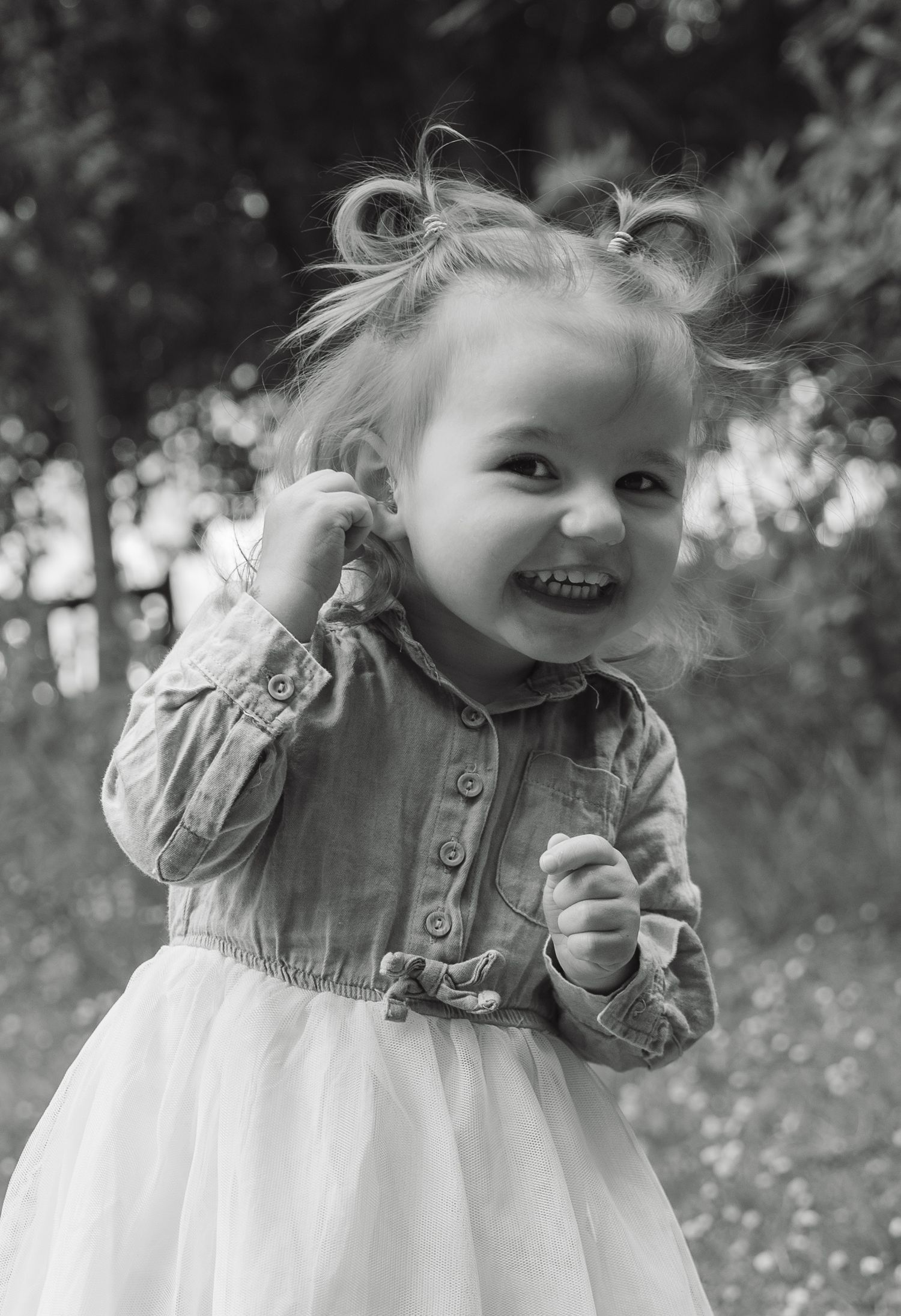 Black and white portrait of a happy toddler girl in a denim top and tulle skirt laughing outdoors.