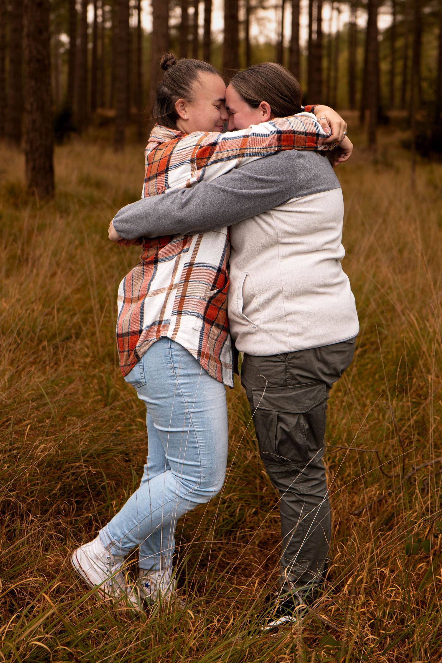Two women sharing a warm embrace while standing in an autumn forest clearing.