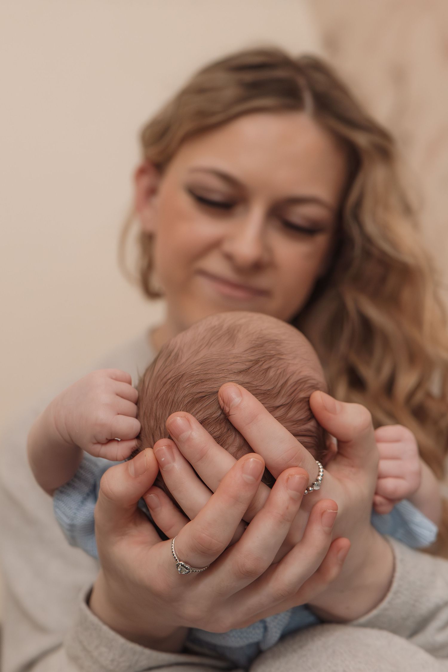Smiling blonde mother tenderly cradling her newborn baby's head in her hands indoors.