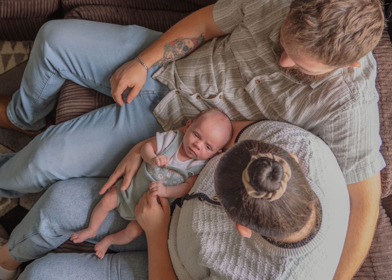 Overhead view of two parents lovingly gazing at their newborn baby on a couch.