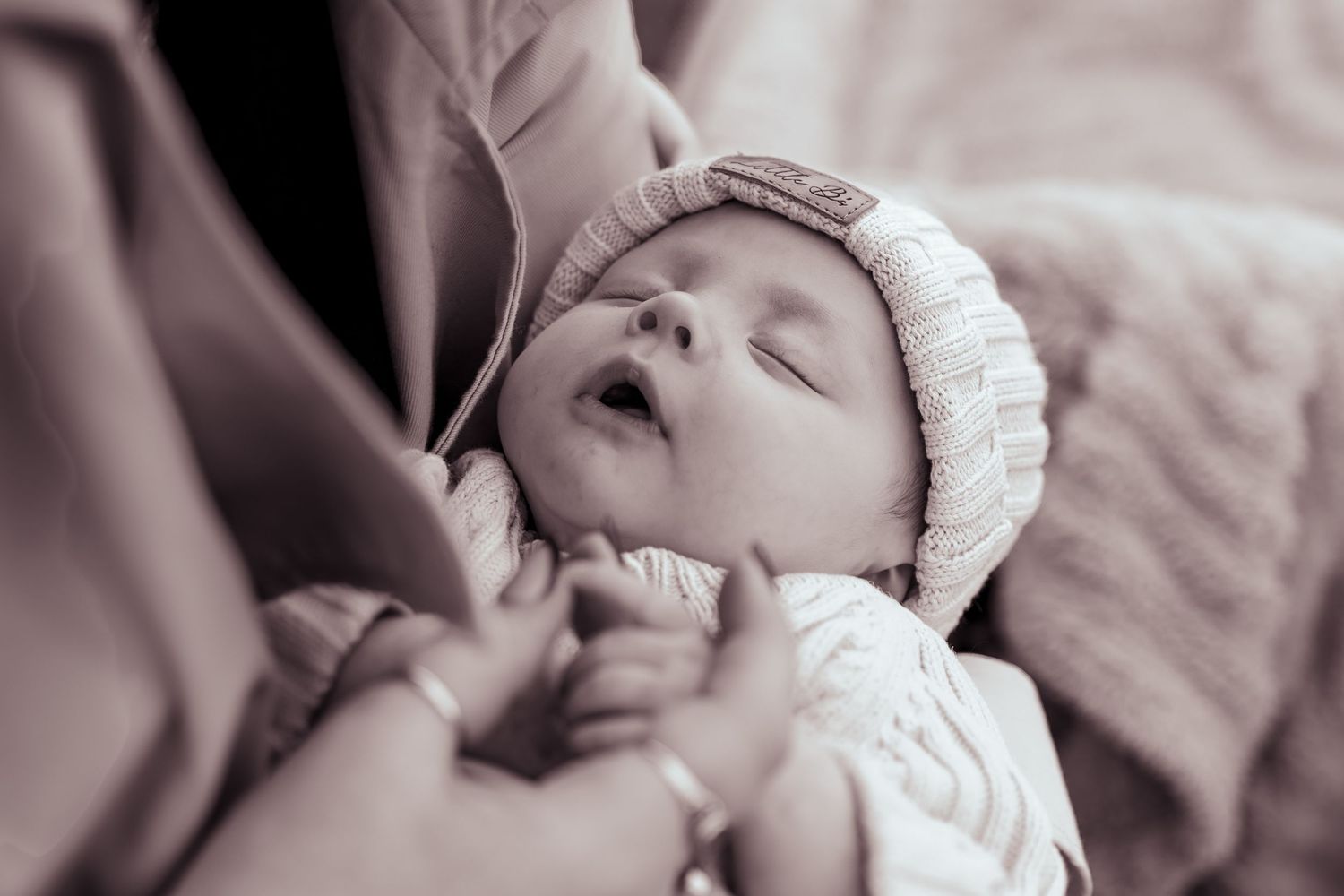 Sepia toned newborn baby sleeping peacefully in a knit hat in parents arms.