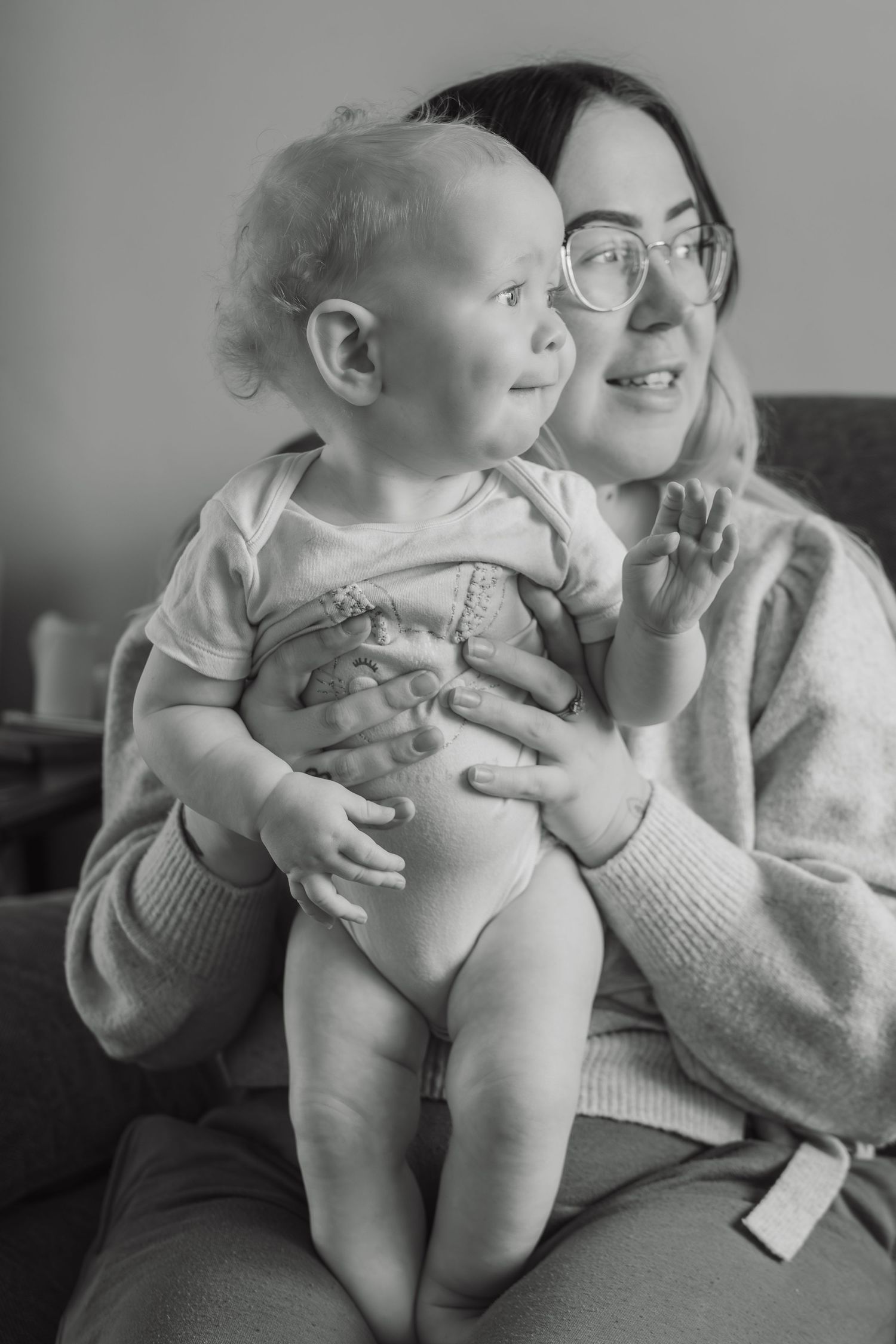 Black and white photo of a smiling mother with glasses holding her happy baby on her lap.