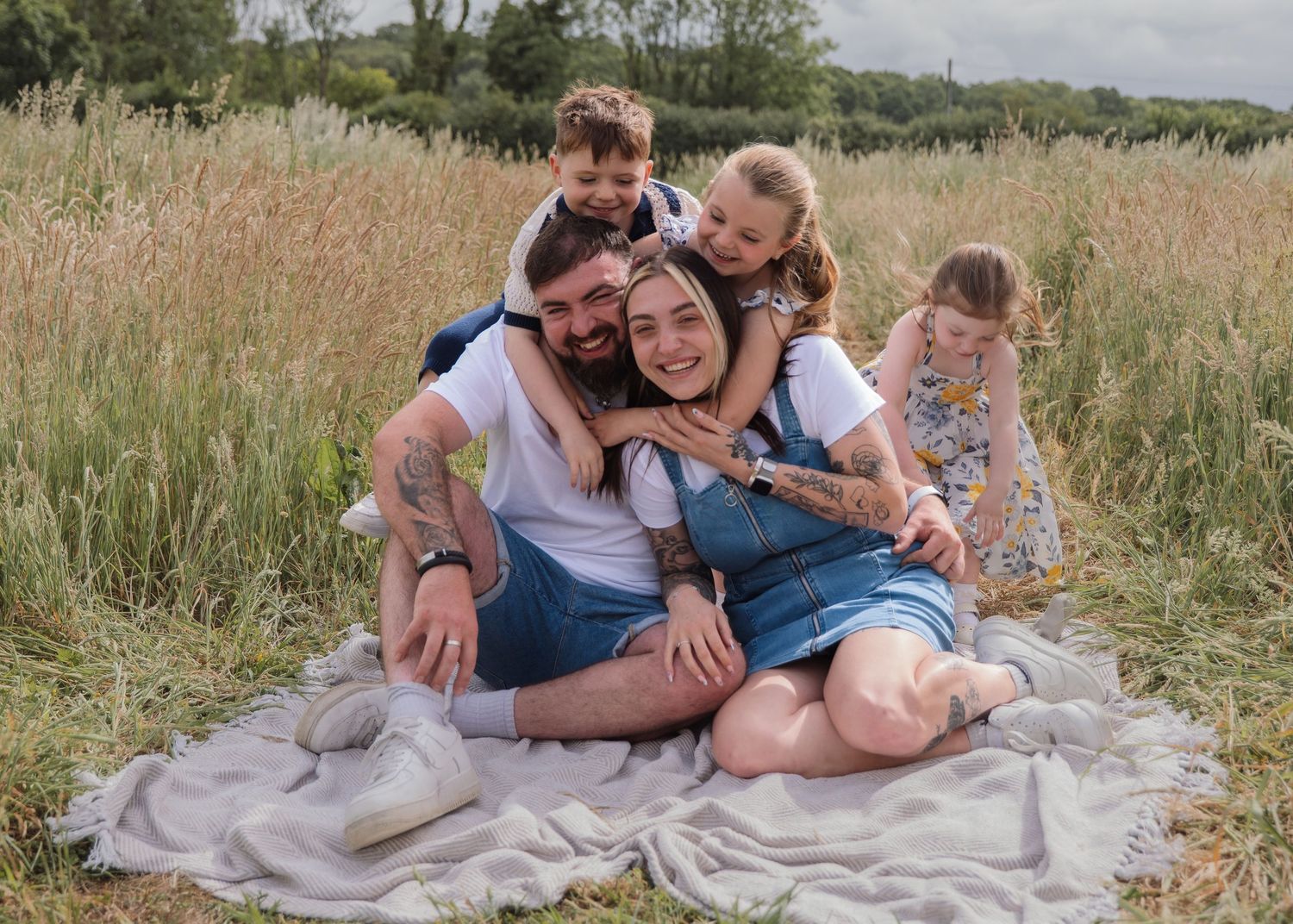 Happy family of five enjoying a outdoor photo session in a golden meadow, sitting together on a blanket.