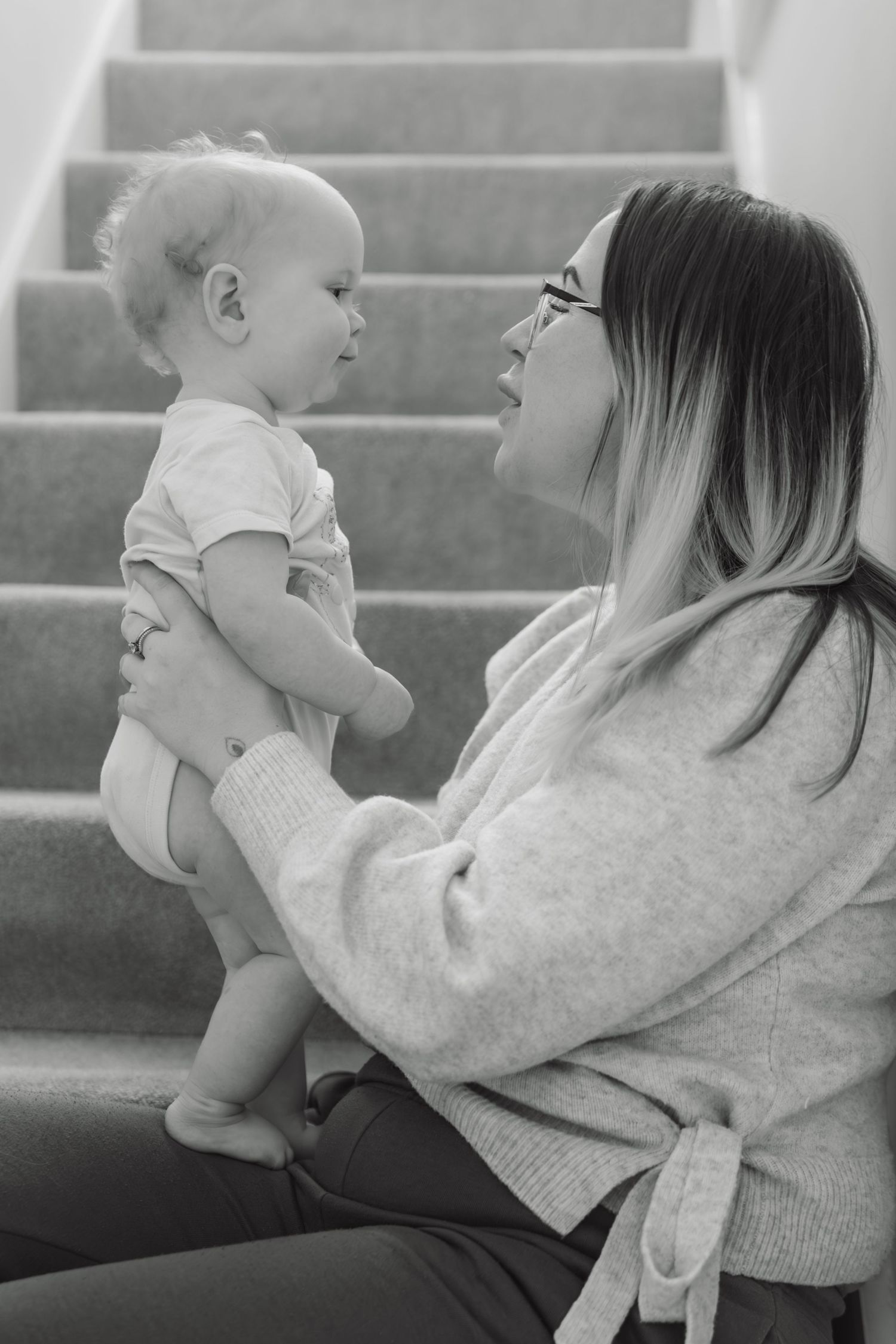 Black and white photo of a mother holding her baby face-to-face while sitting on stairs.