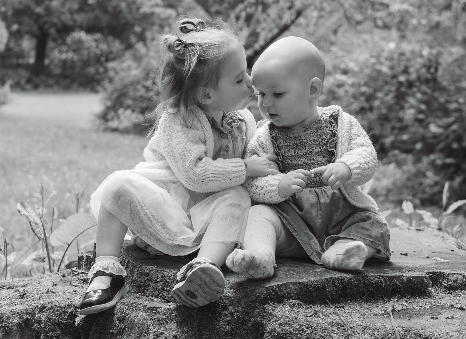 Two young children sharing a sweet moment on a rock outdoors in a classic black and white photo.