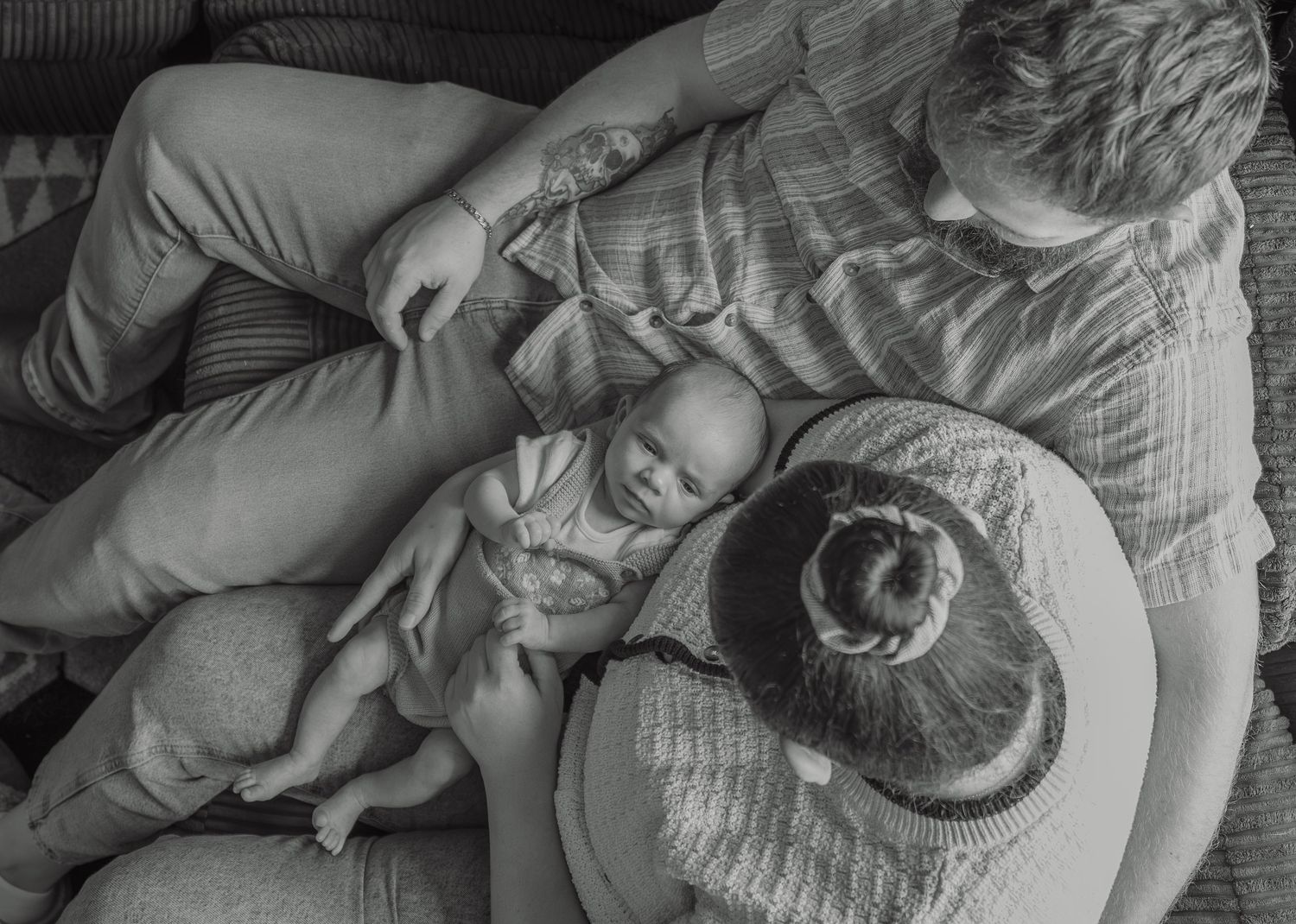 Black and white photo of parent cradling newborn baby on a couch, viewed from above.