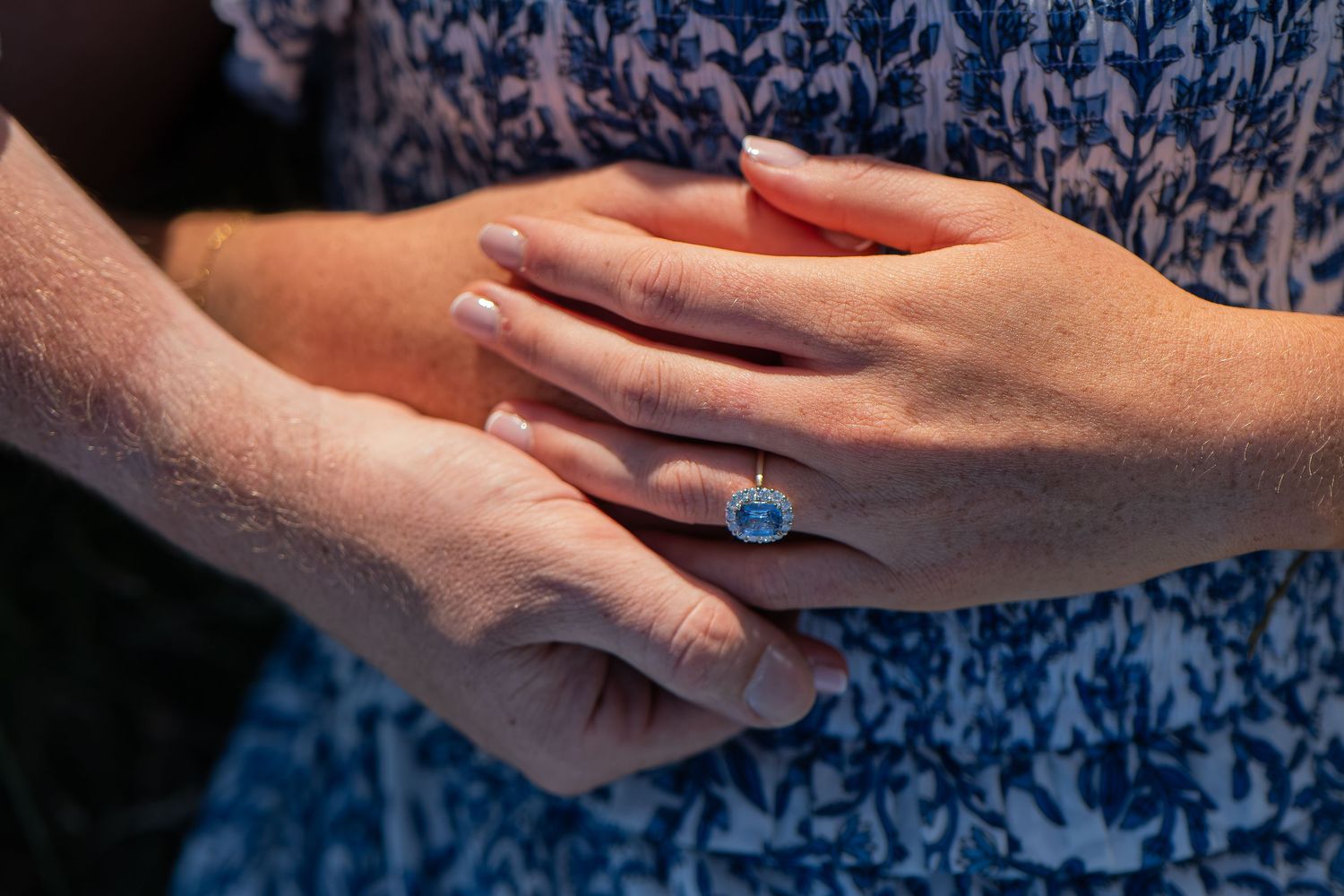 Close-up of hands showing a stunning blue gemstone ring in a gold bezel setting on a woman's finger.