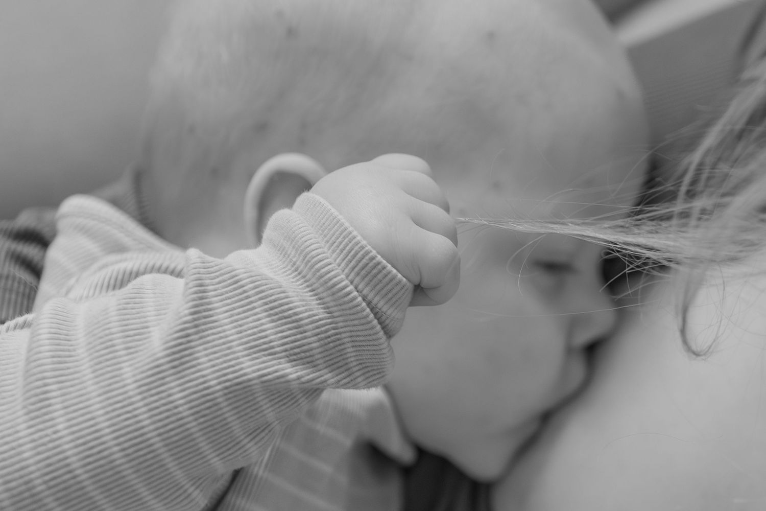 Black and white photo of a sleeping baby in striped onesie gently touching a toddler's hair.