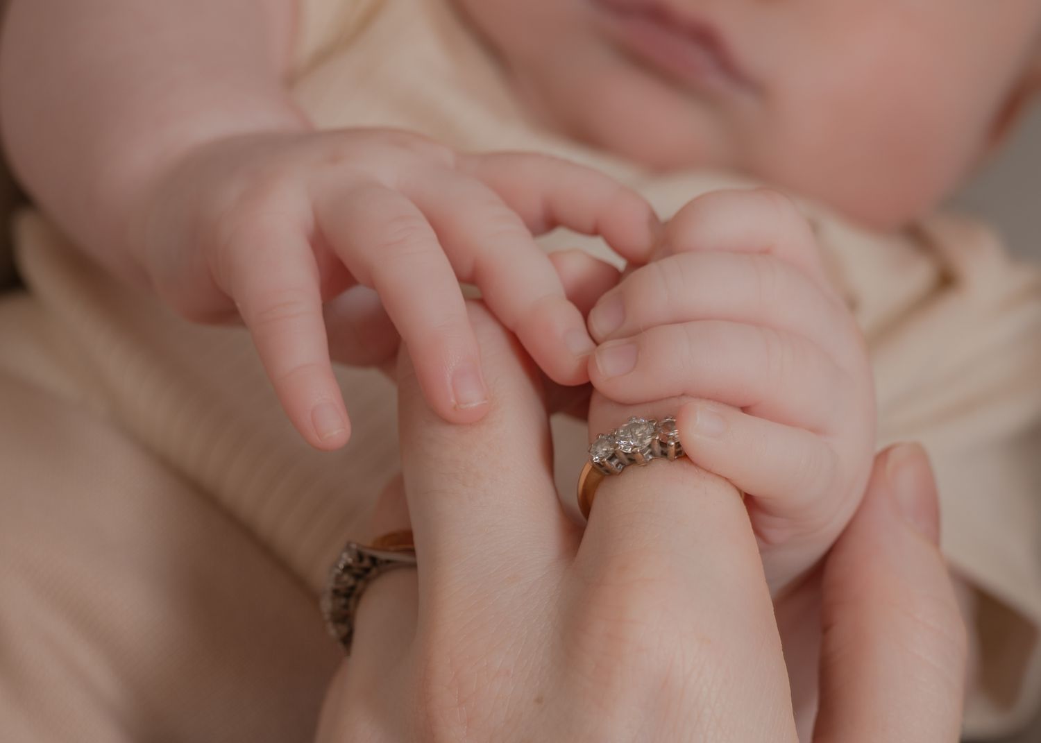 A newborn baby grasping a mother's finger adorned with a diamond engagement ring, close-up tender moment.
