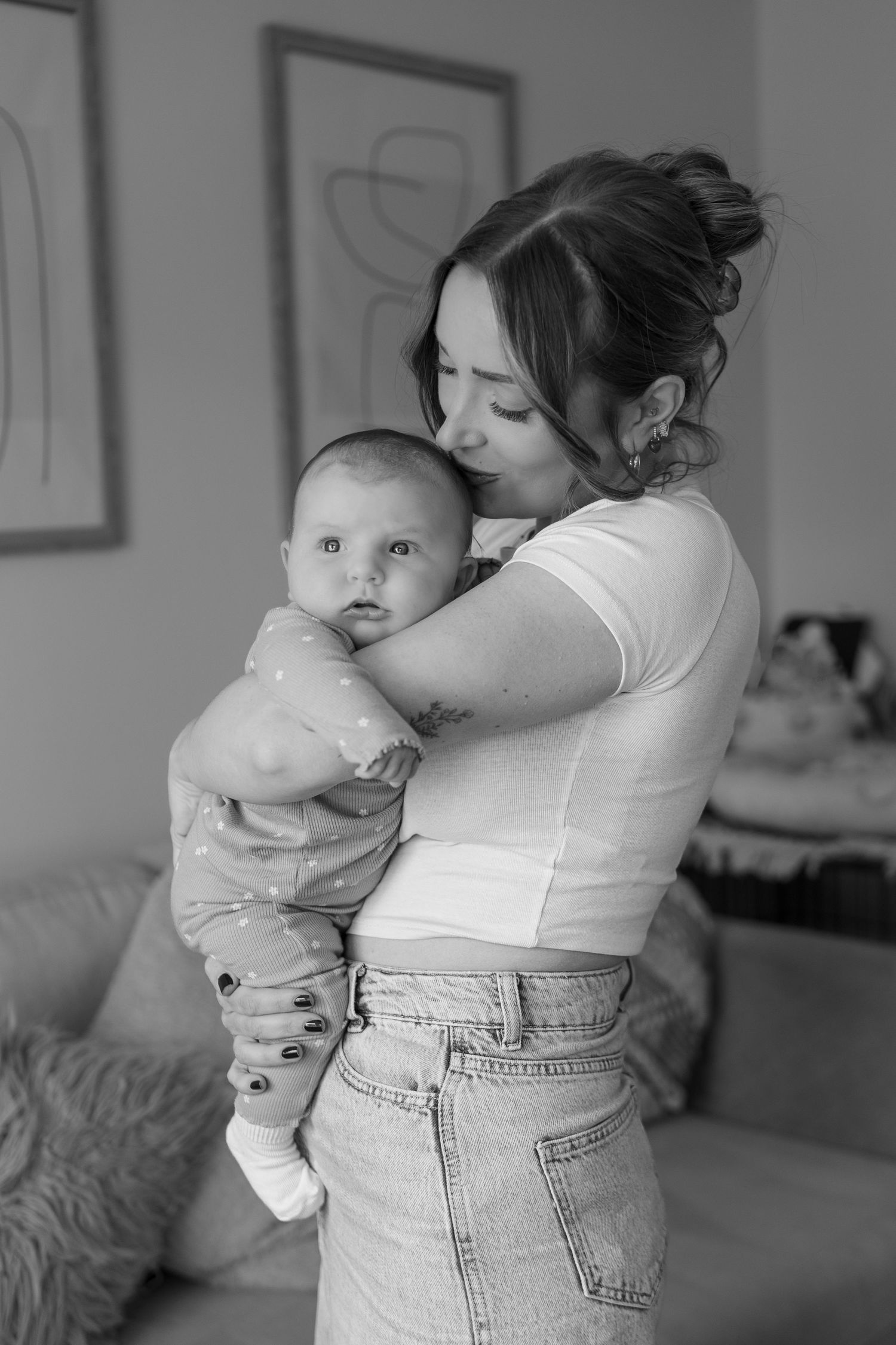 Black and white image of mother kissing her baby during documentary style photoshoot at home