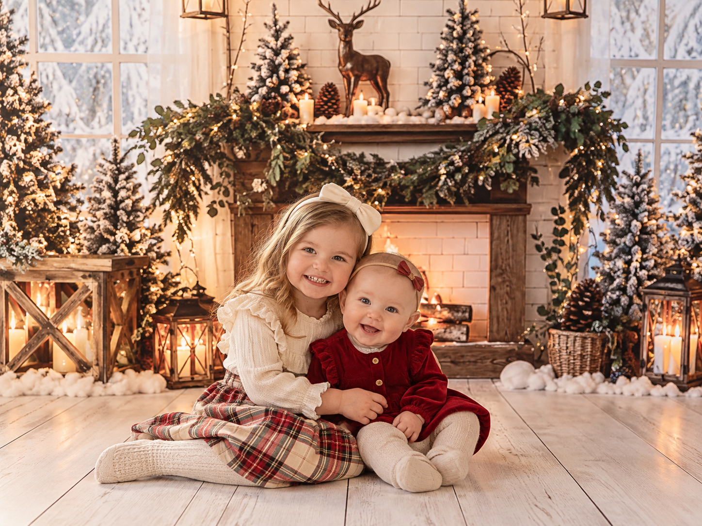 Two children pose in a festive Christmas setting with lit trees, lanterns, and a decorated fireplace mantel.