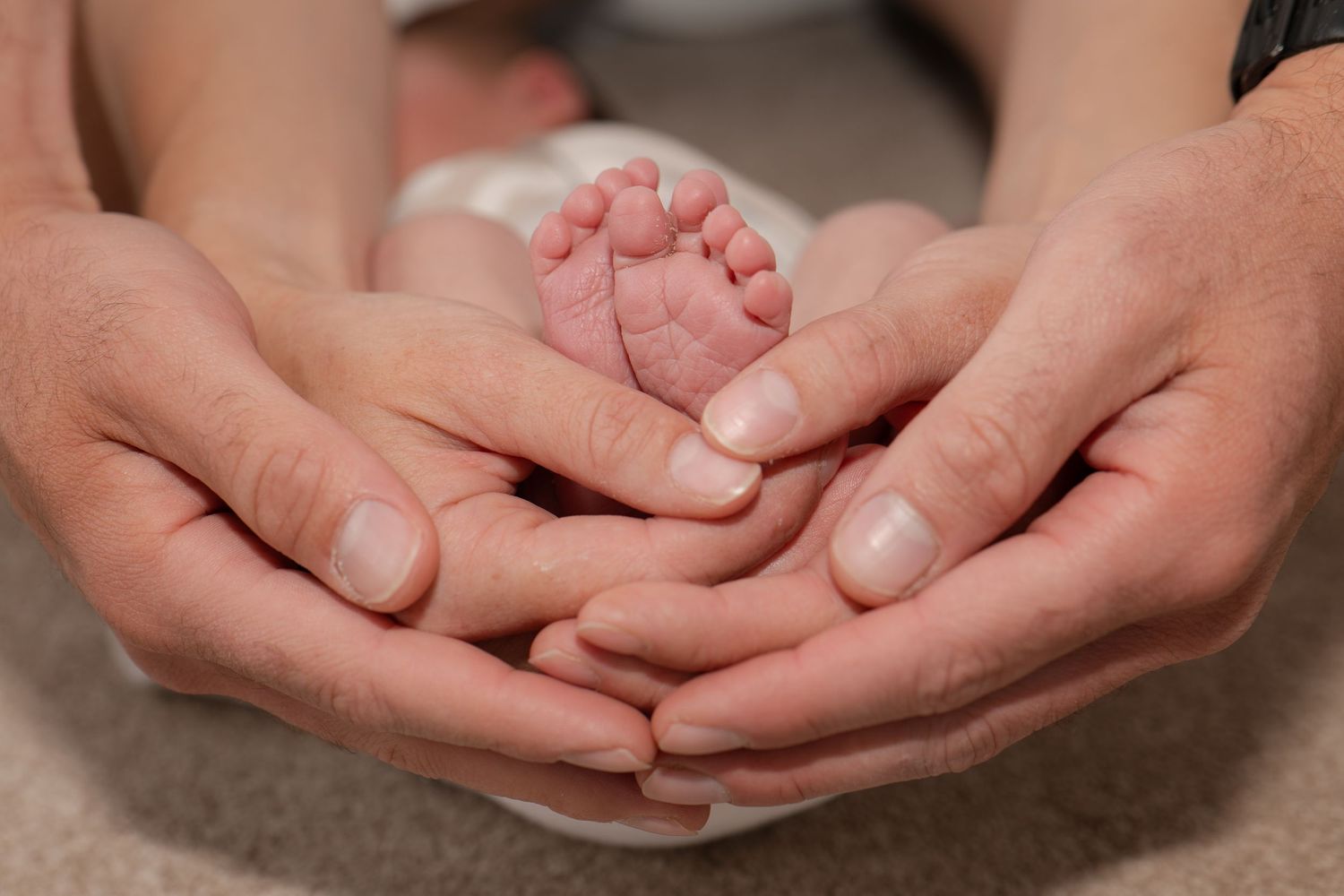 Two adult hands cradling tiny newborn baby feet, symbolizing love and parental care.