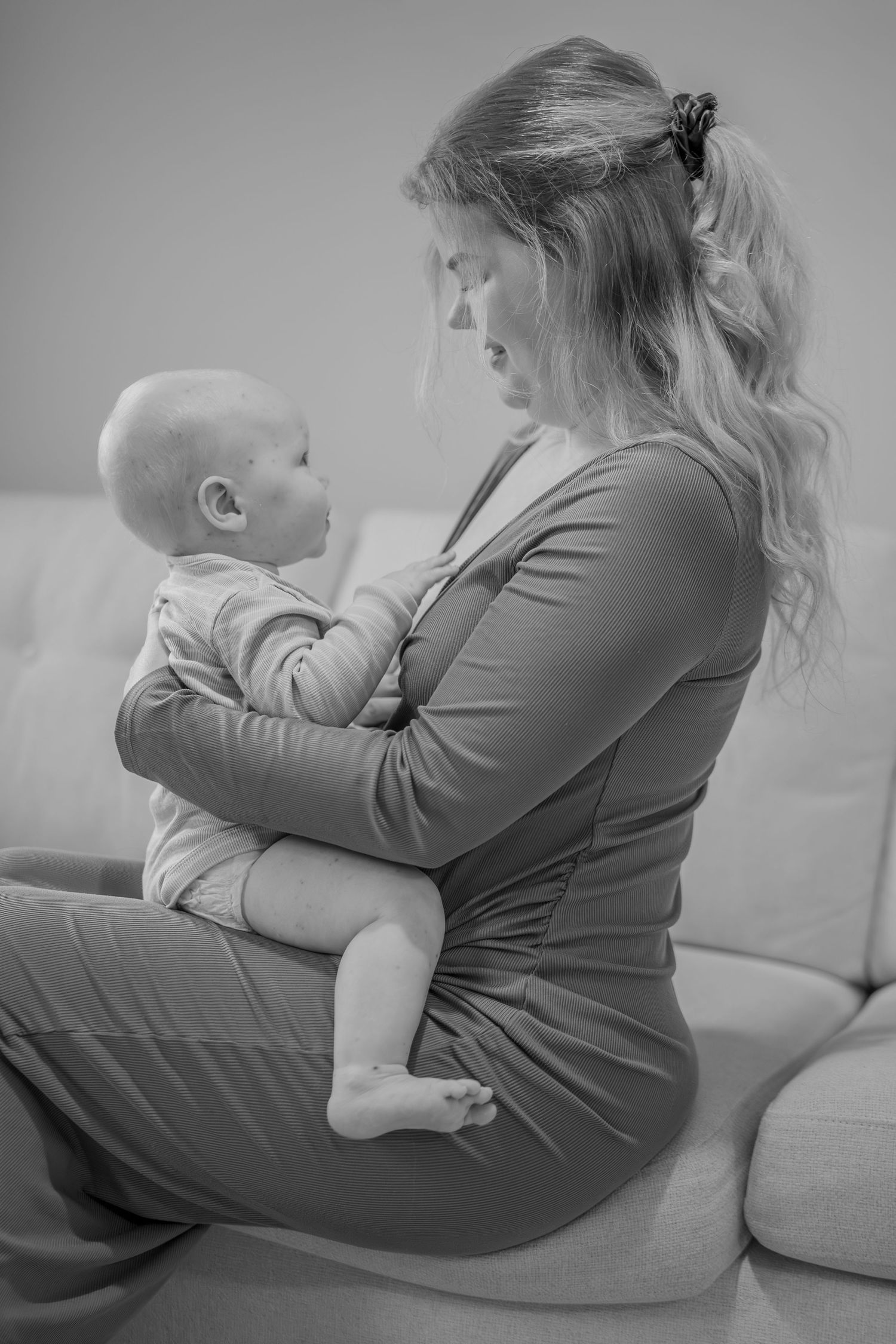 Black and white photo of a young mother sitting on a sofa, tenderly holding her baby in her arms.