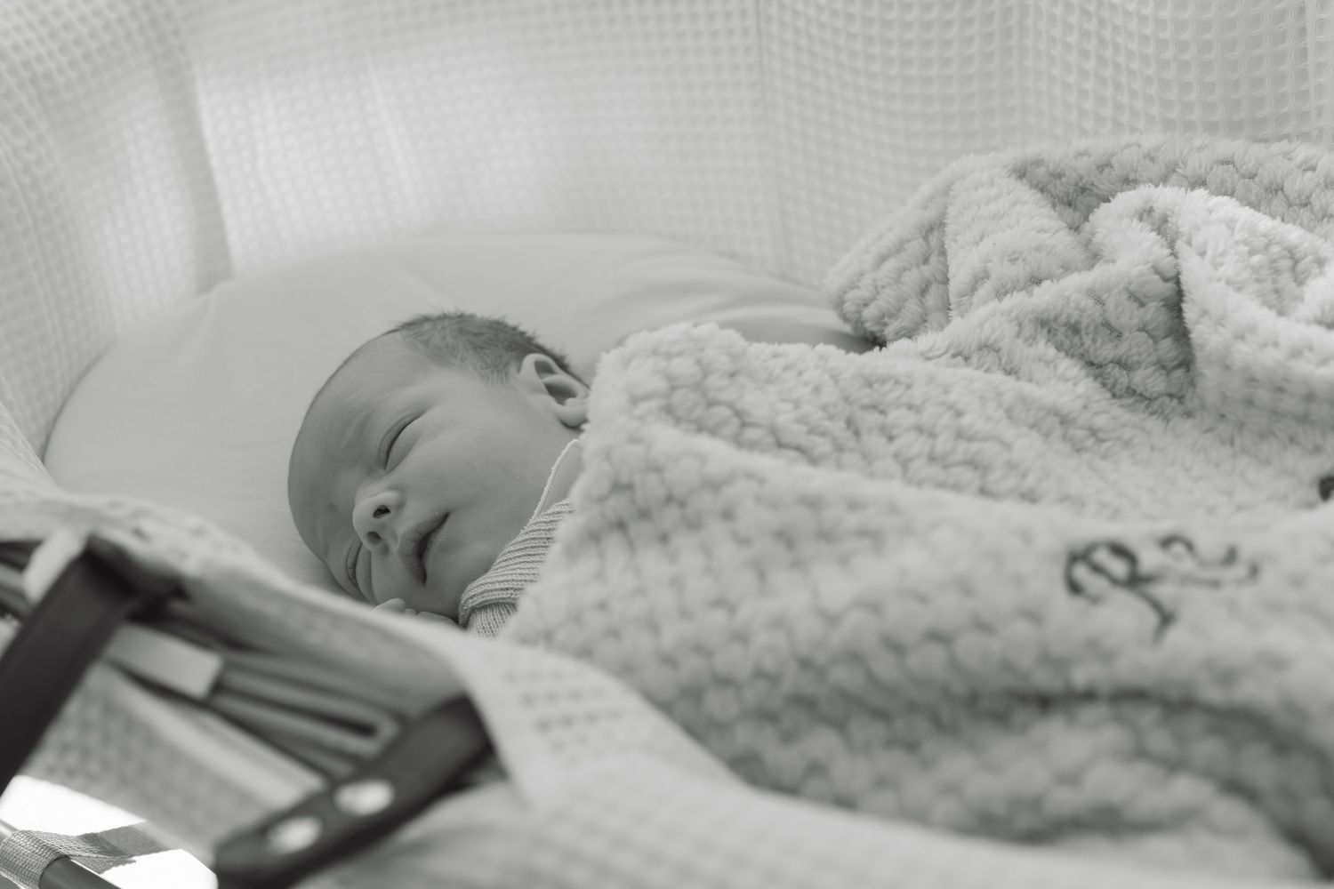 Newborn baby sleeping peacefully wrapped in a white waffle knit blanket in a hospital bassinet.