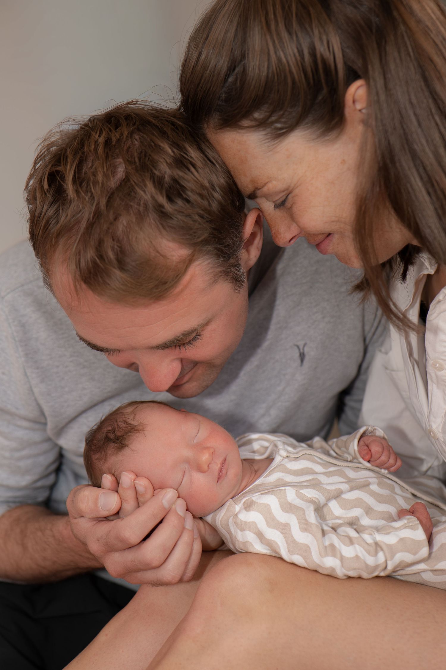 New parents lovingly gaze at their sleeping newborn baby, sharing a tender family moment together.