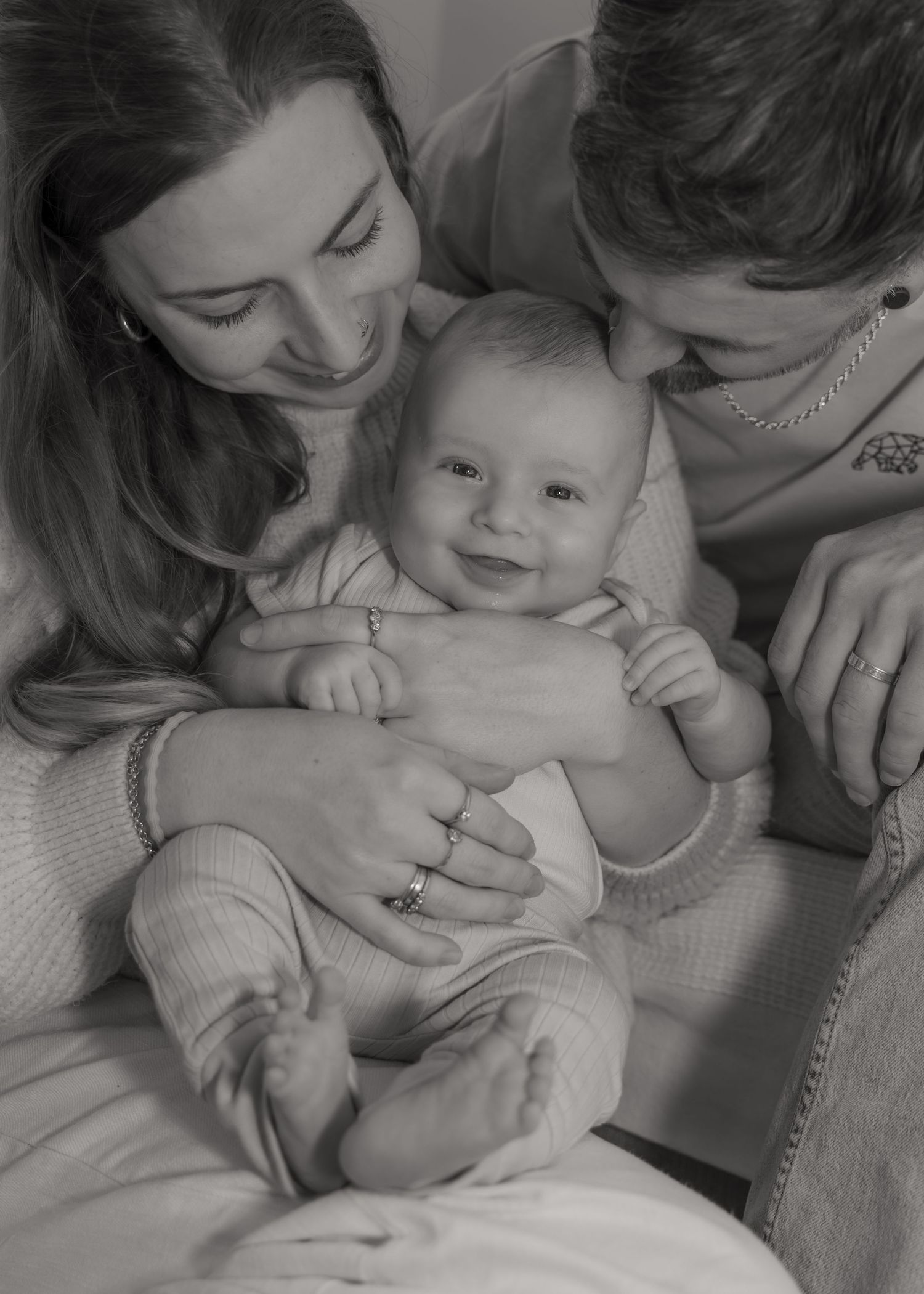 Black and white photo of smiling parents lovingly holding their happy newborn baby together.