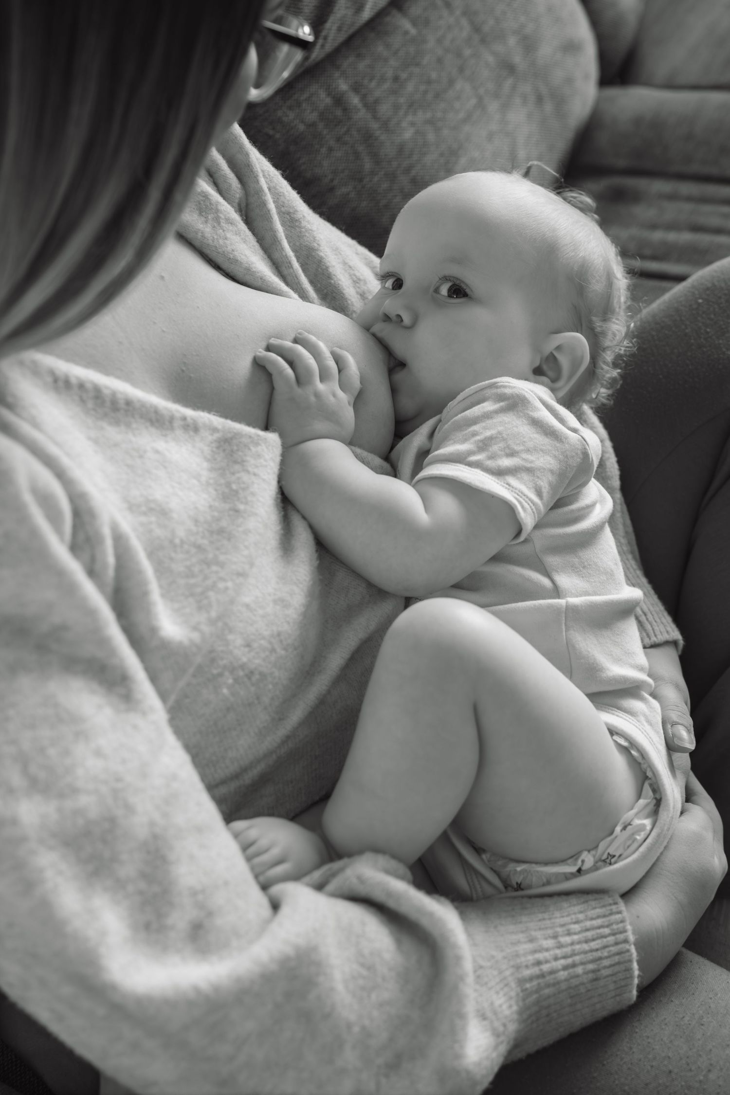 Black and white photo of a mother breastfeeding her infant baby on a couch at home.