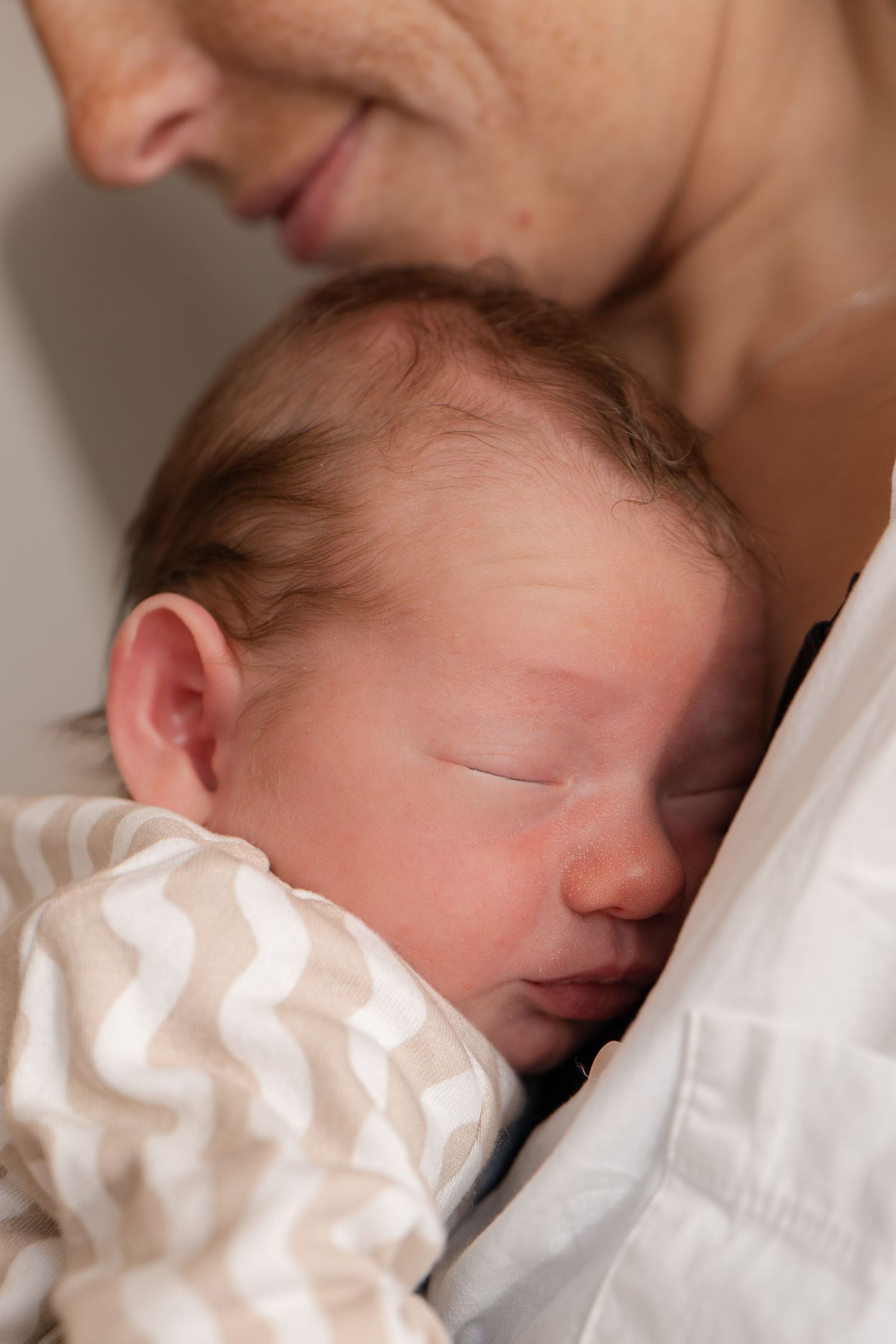 Close-up of a sleeping newborn baby in a chevron outfit nestled against a parent's chest.