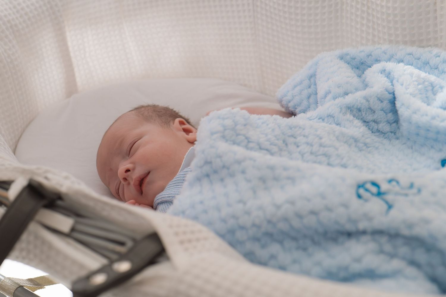 Newborn baby sleeping wrapped in a soft blue waffle blanket in a hospital bassinet.