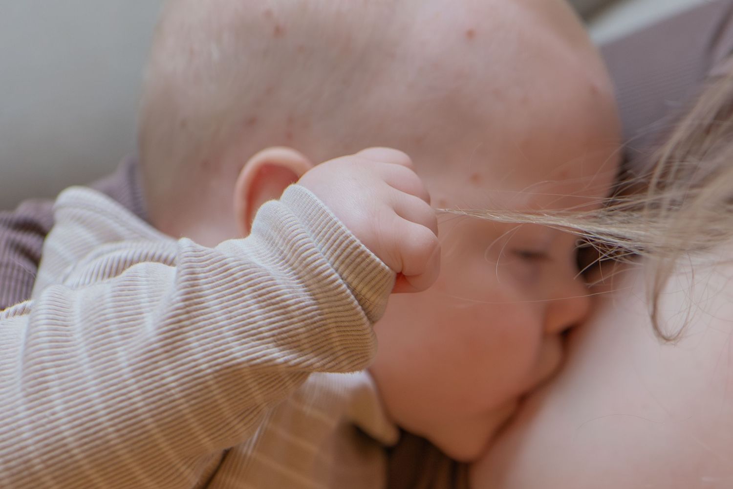 Close-up of a newborn baby breastfeeding, grasping mothers hair gently.