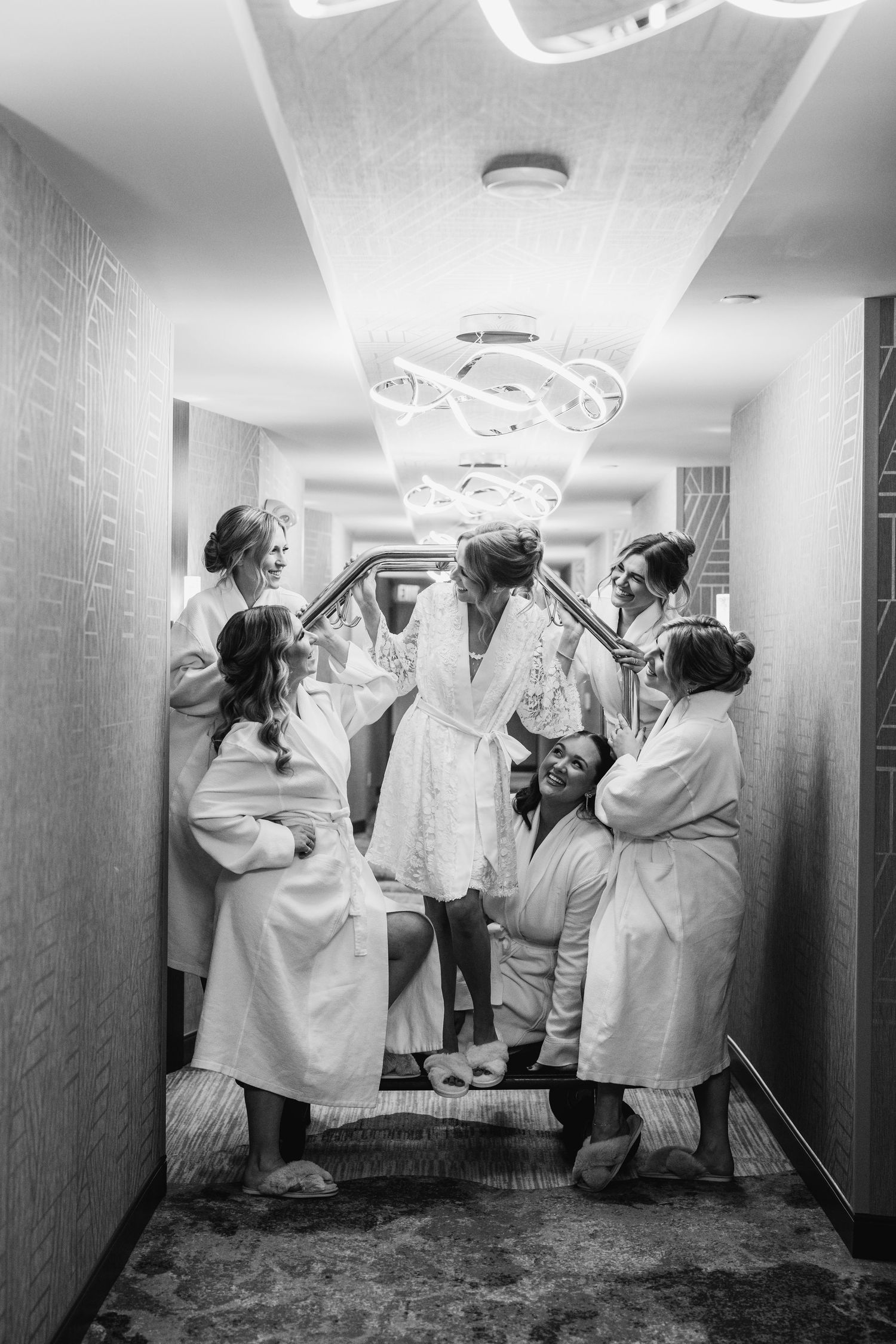 Black and white photo of bride and bridesmaids in robes gathered in hotel hallway getting ready.