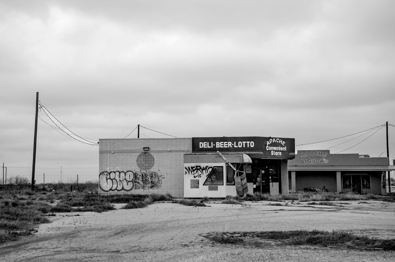Black and white photo of an abandoned rural deli and lotto store under overcast skies.