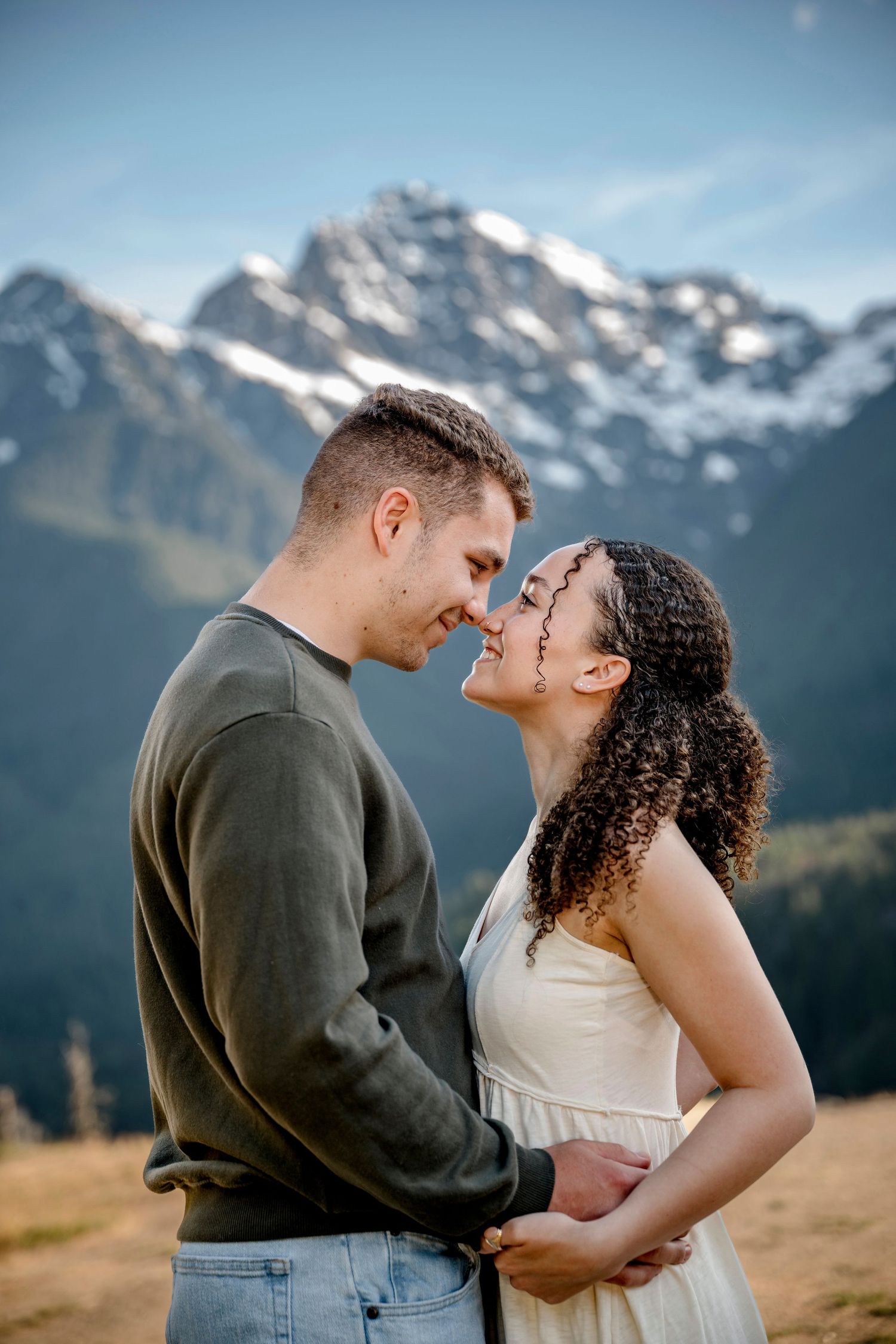Couple sharing a romantic moment with snow-capped mountains backdrop during an outdoor engagement photo session.