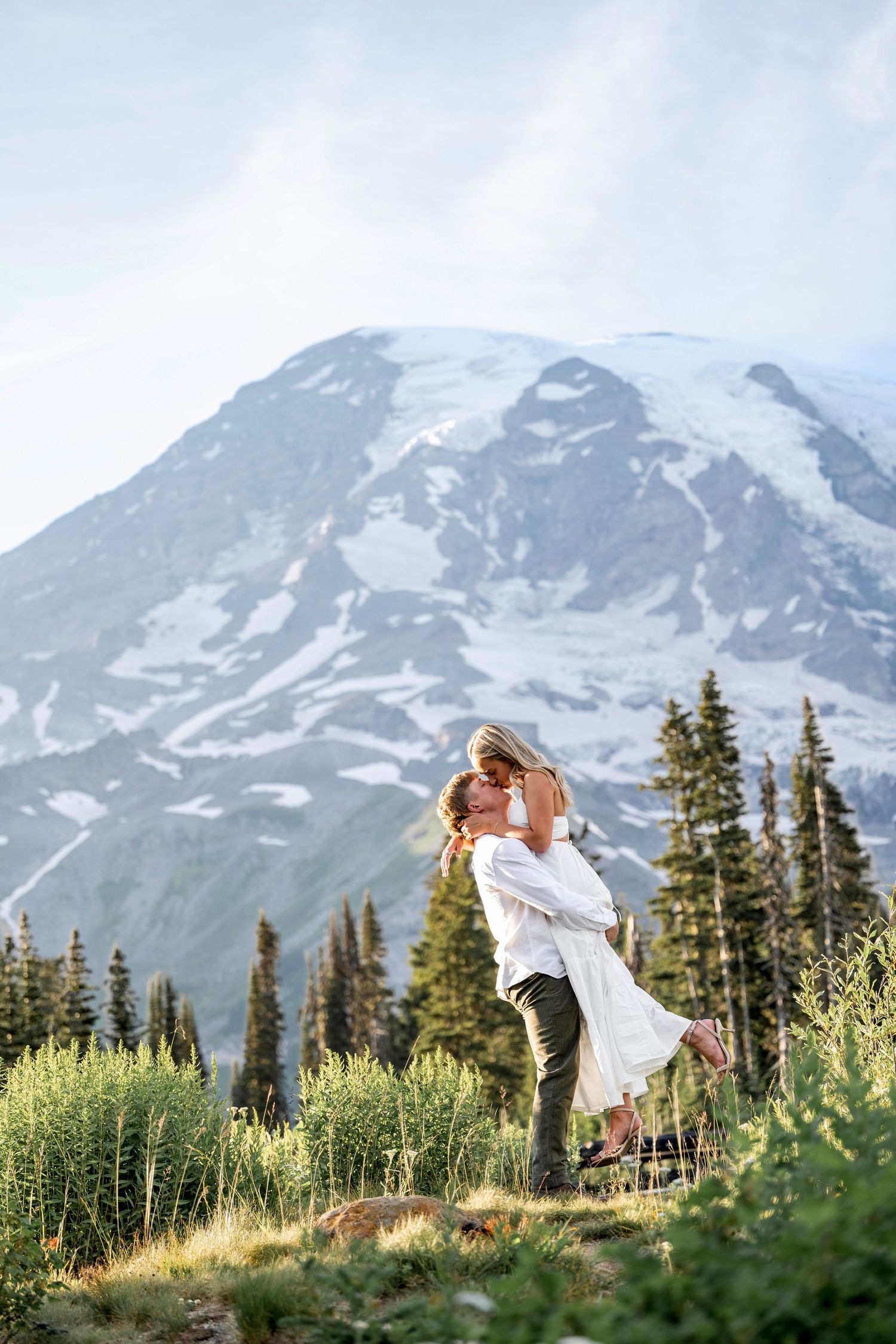 Couple embracing with snow-capped Mount Rainier and evergreen trees in background.