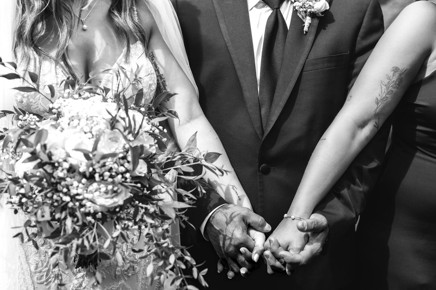 Black and white photo of bride and groom holding hands, bride holding floral bouquet.