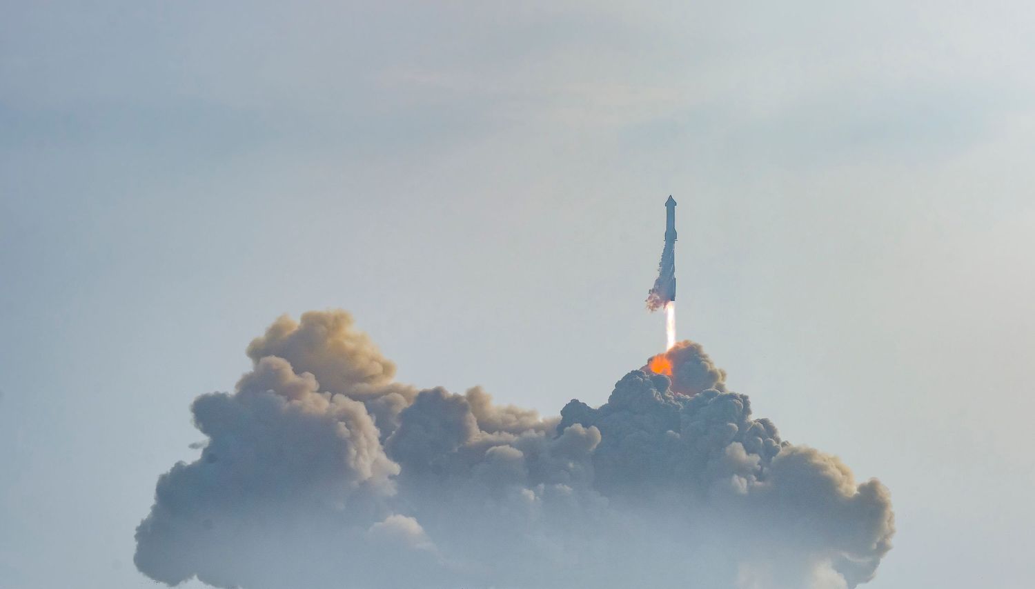 A rocket launches through thick clouds of smoke and steam at a space launch facility.
