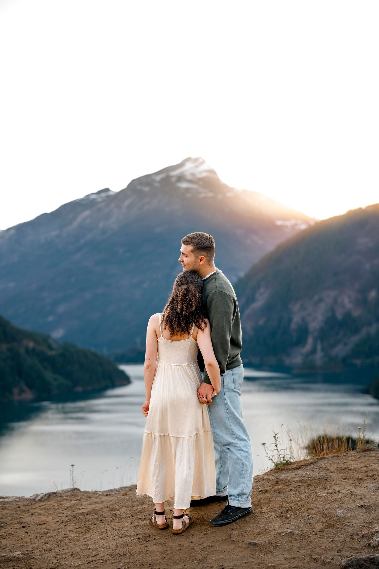 Couple holding hands overlooking a serene mountain lake at sunset in the Pacific Northwest.