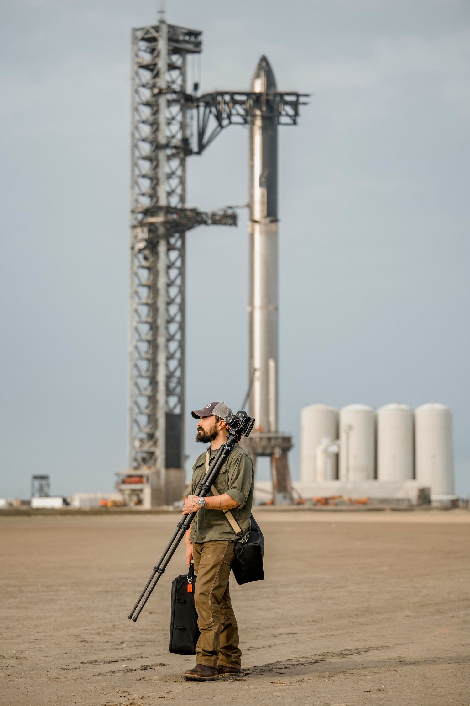 Photographer with tripod stands before SpaceX Starship rocket on launch pad at Starbase, Texas.