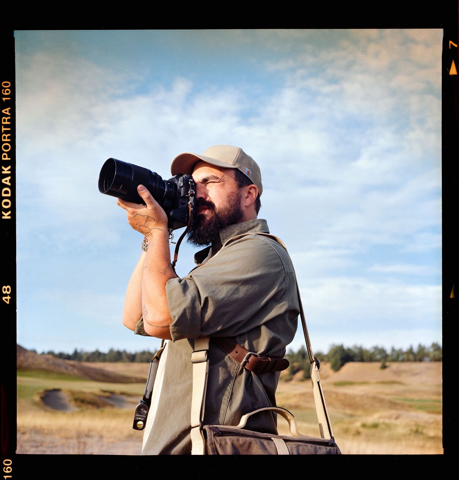 Bearded photographer capturing shots with a professional camera outdoors on Kodak Portra film.