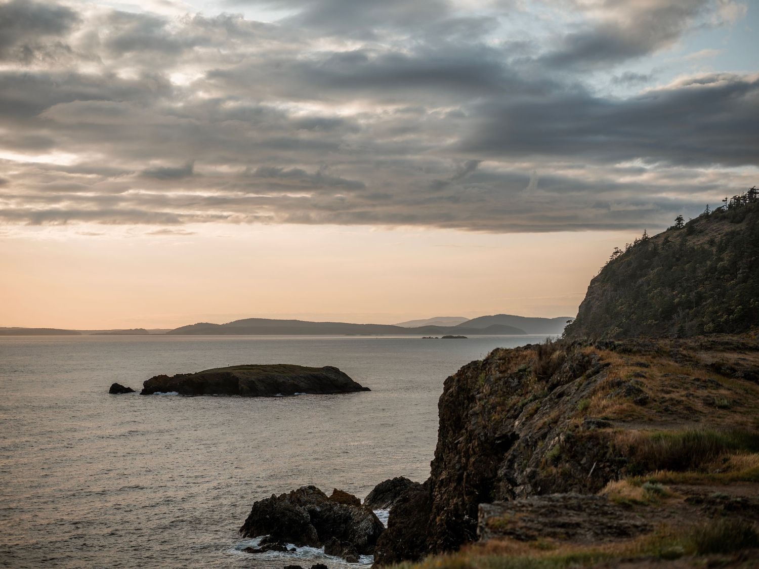 Dramatic coastal cliffs and rocky sea stacks at sunset under a cloudy sky.