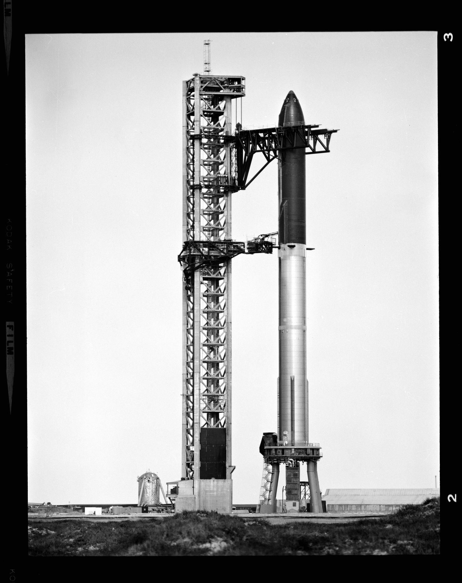 Black and white photo of SpaceX Starship rocket on launch pad with tall integration tower at Boca Chica, Texas.