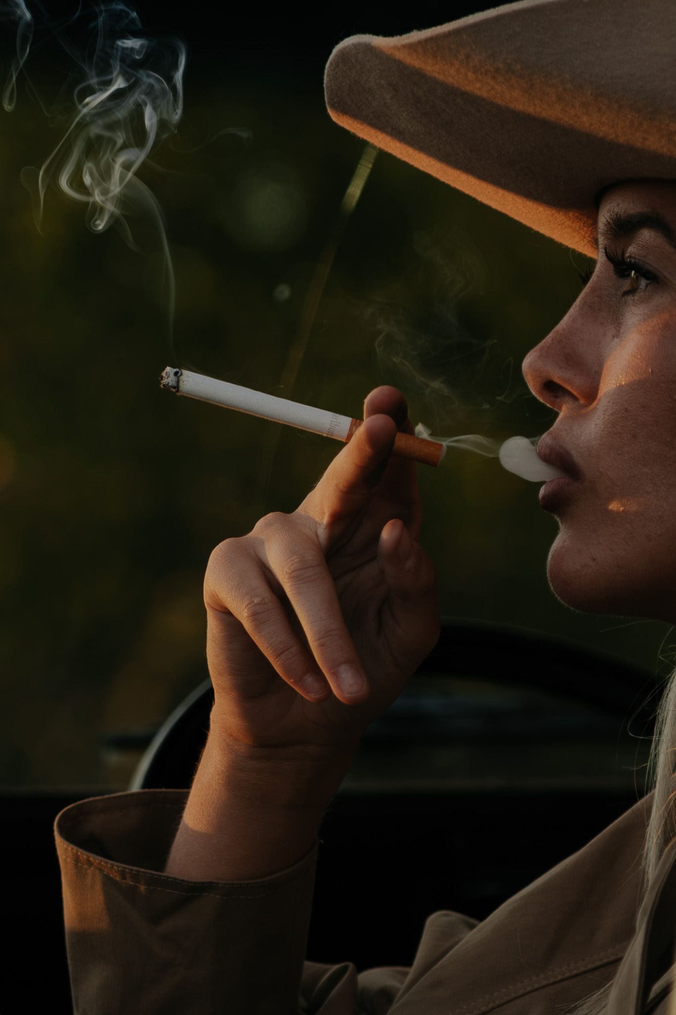 Close-up of woman in cowboy hat exhaling cigarette smoke in dramatic low-light setting.