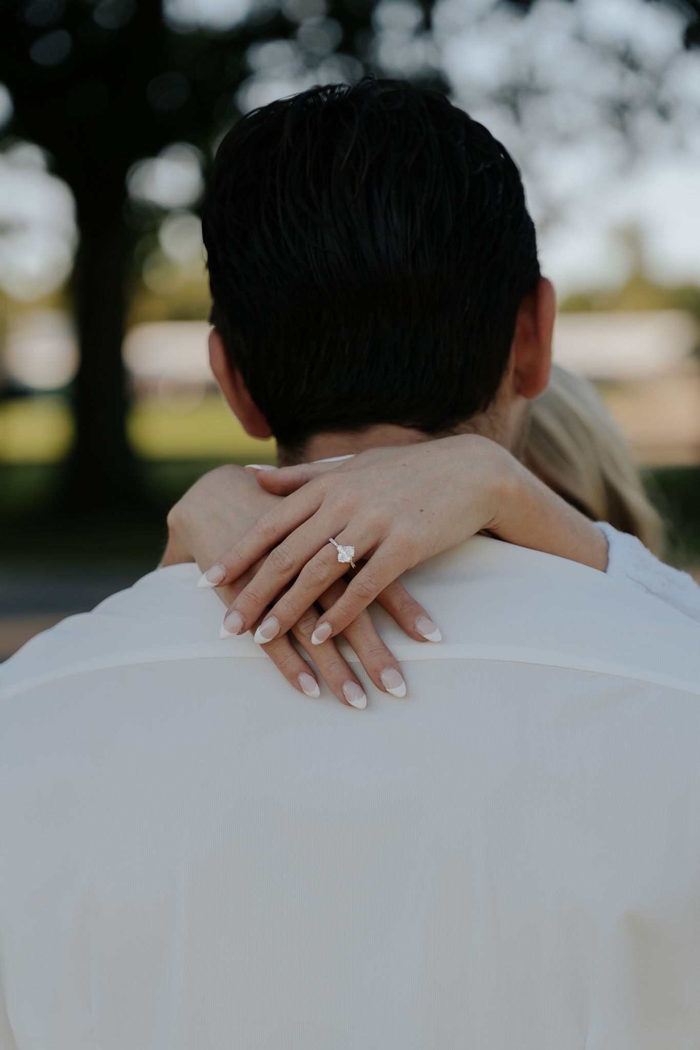 Close-up of a woman's hand with an engagement ring resting on her partner's shoulder.